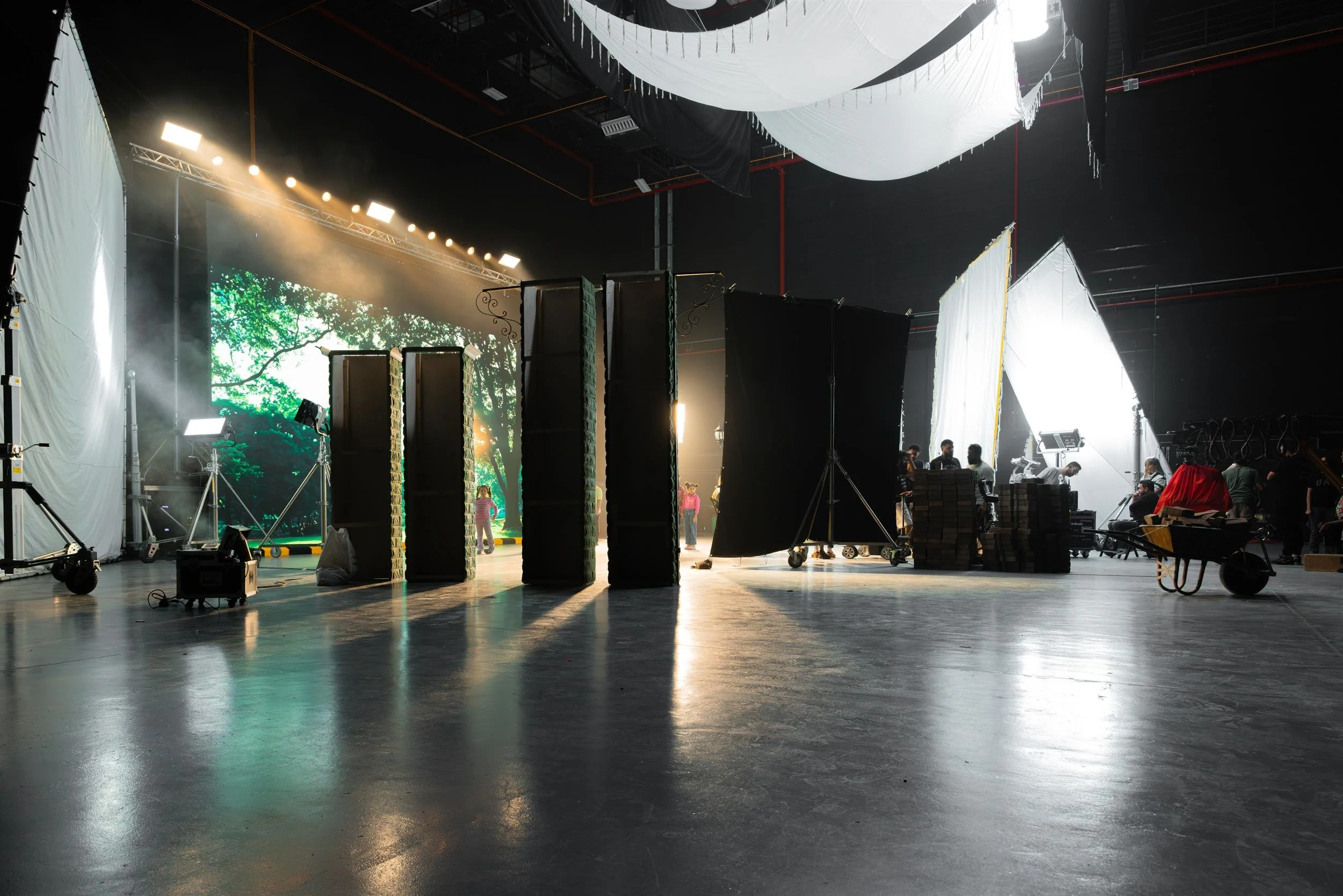 Ahlan Simsim unit still: Green set pillars stand before a forest LED screen in a dark studio filled with lighting gear.