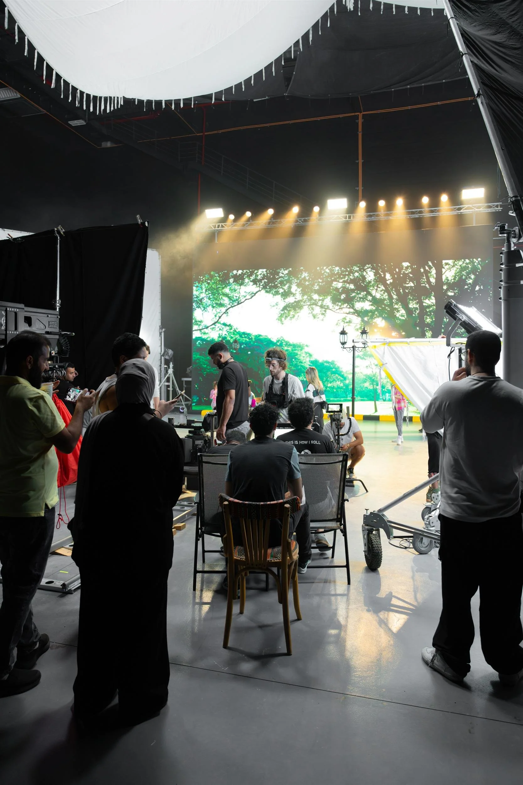 Ahlan Simsim unit still: Production crew members work in a studio in front of a large screen showing a bright park scene.