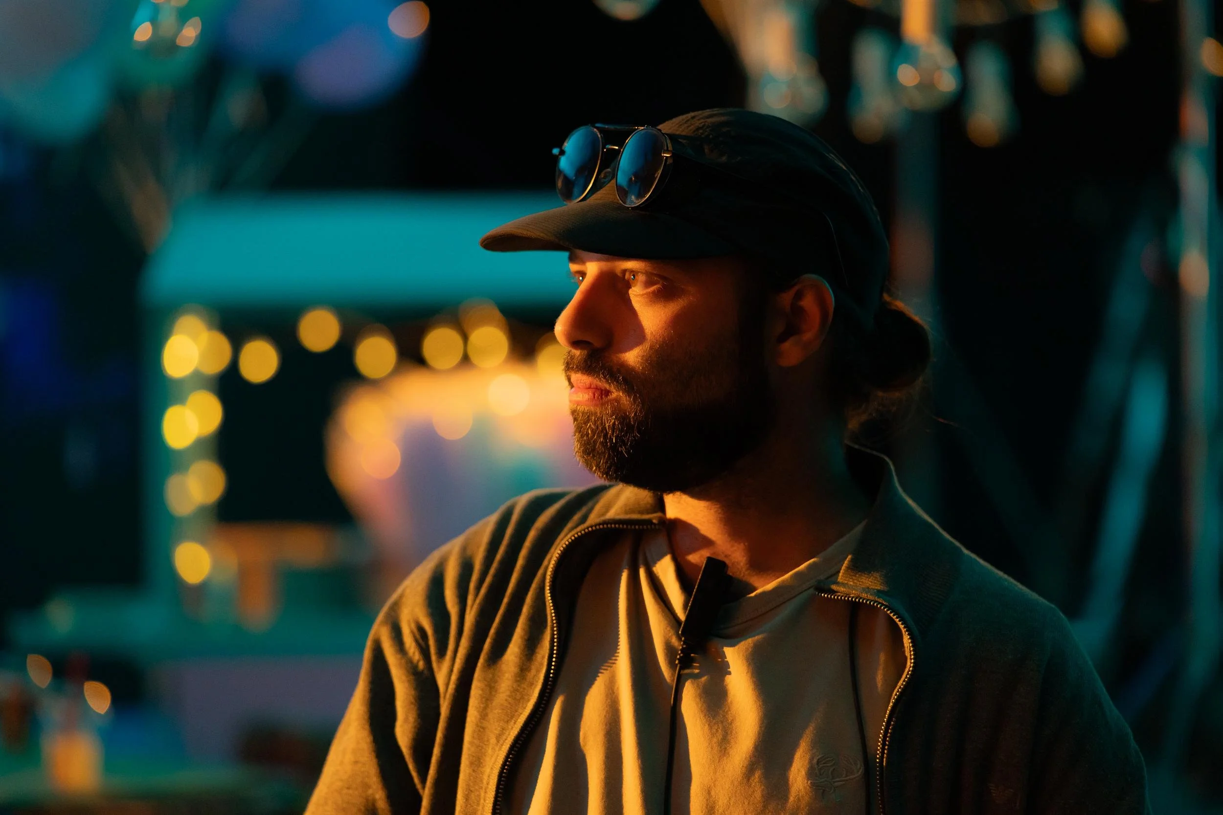 Ahlan Simsim unit still: a bearded crew member in profile under warm light with a night-market set behind him.