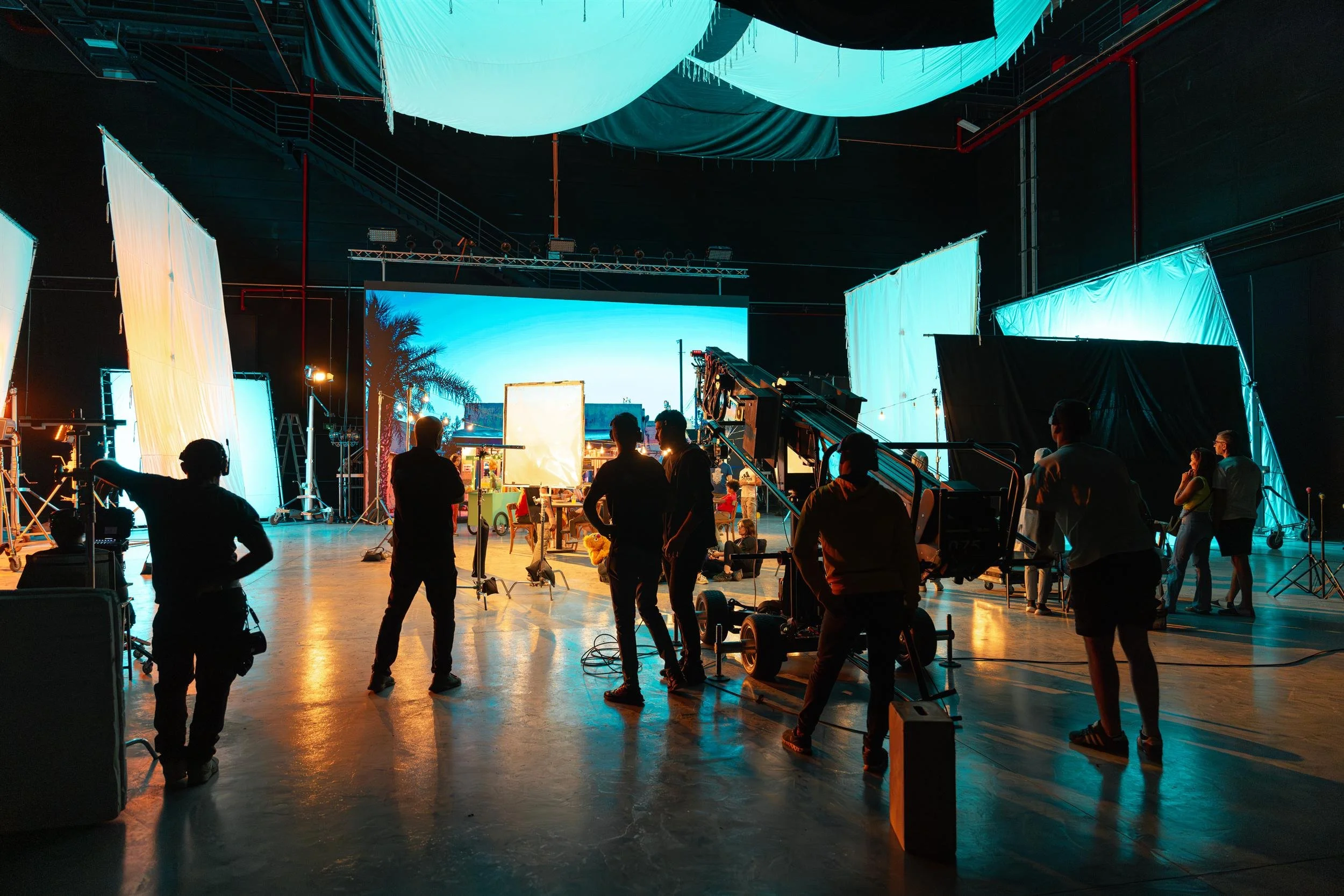 Ahlan Simsim unit still: crew silhouettes and a camera crane face a bright LED backdrop on a large soundstage.