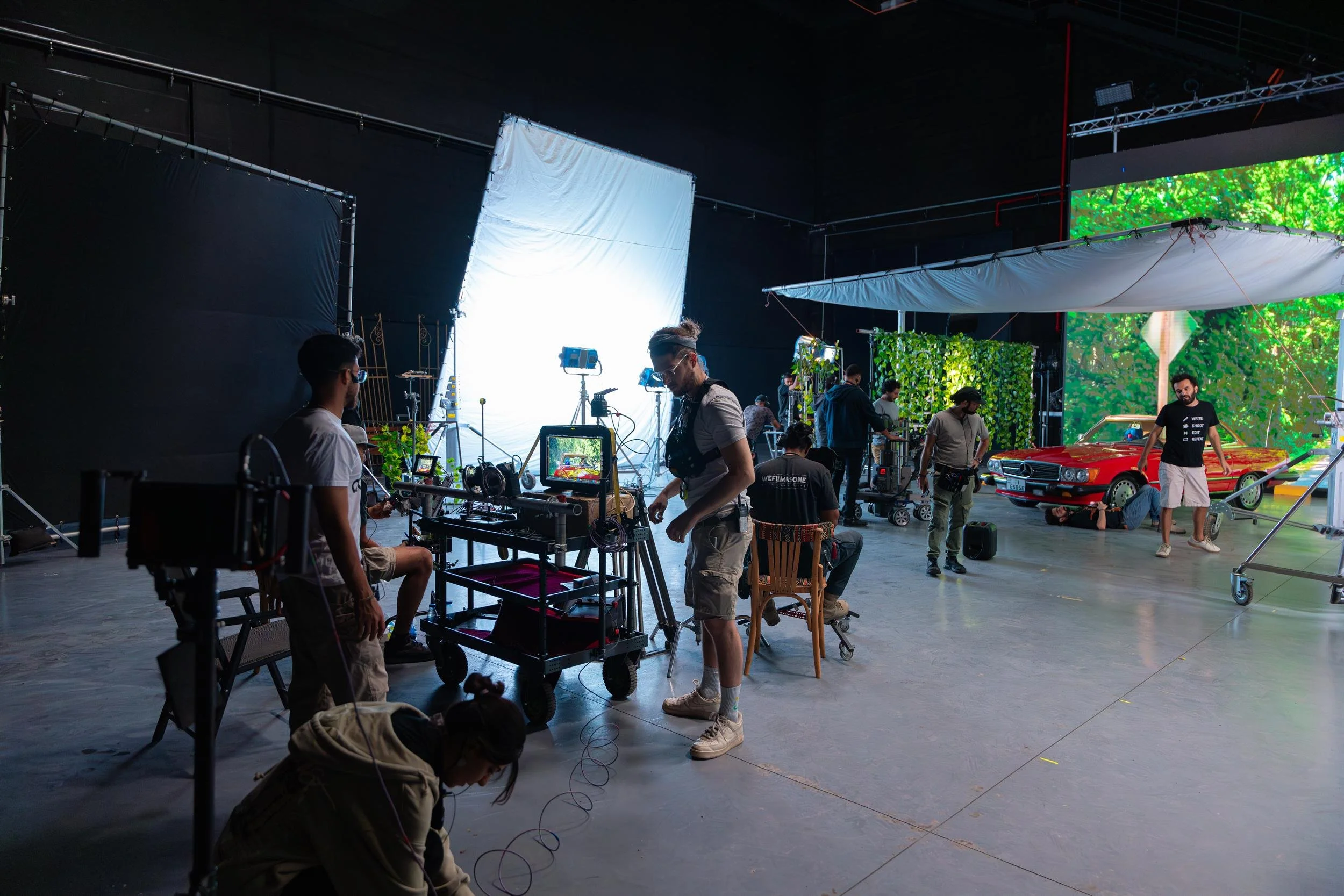 Ahlan Simsim unit still: crew work around a vintage red car on a studio set with an LED forest backdrop.
