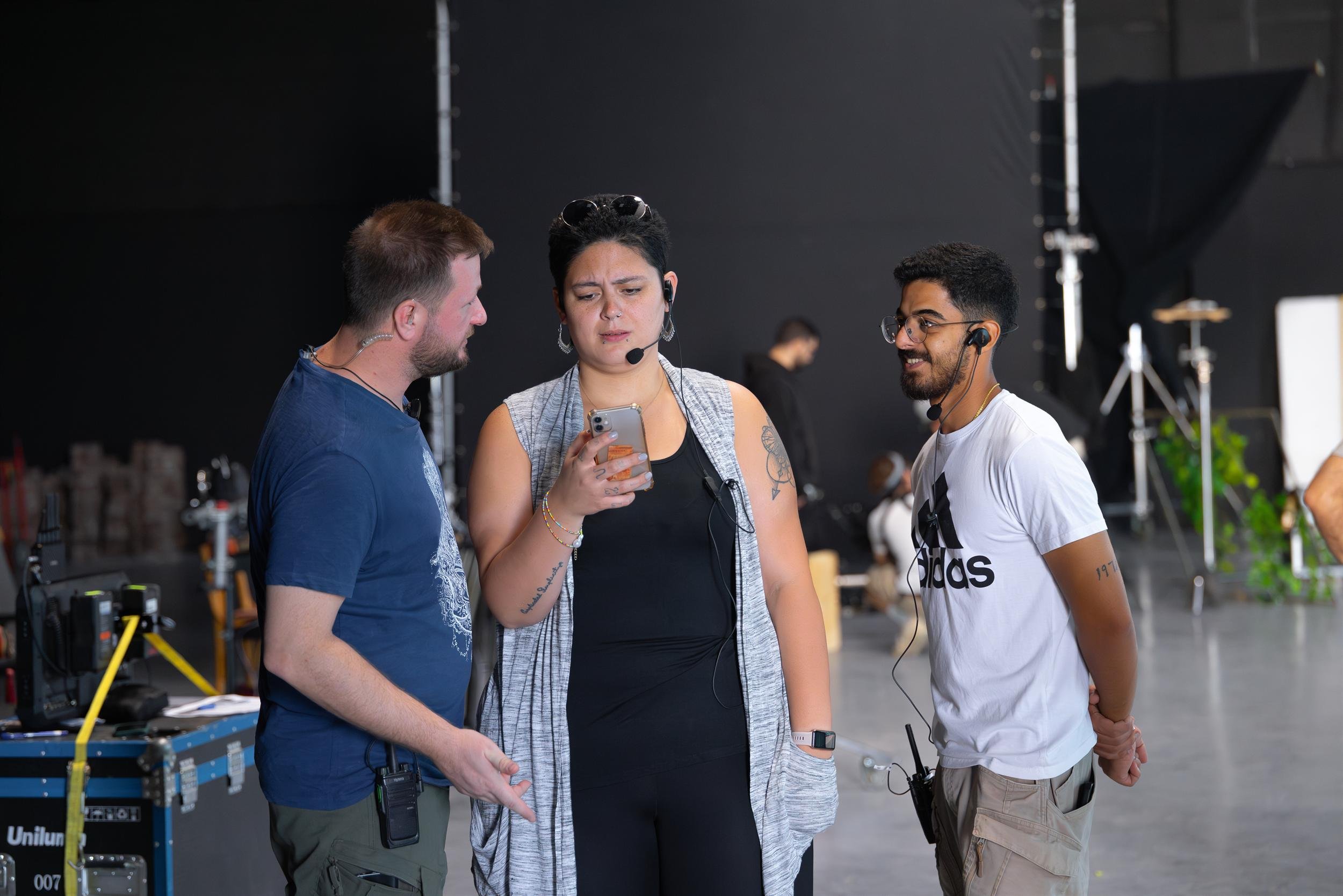 Ahlan Simsim unit still: three crew members in headsets discuss a phone screen on the studio floor.