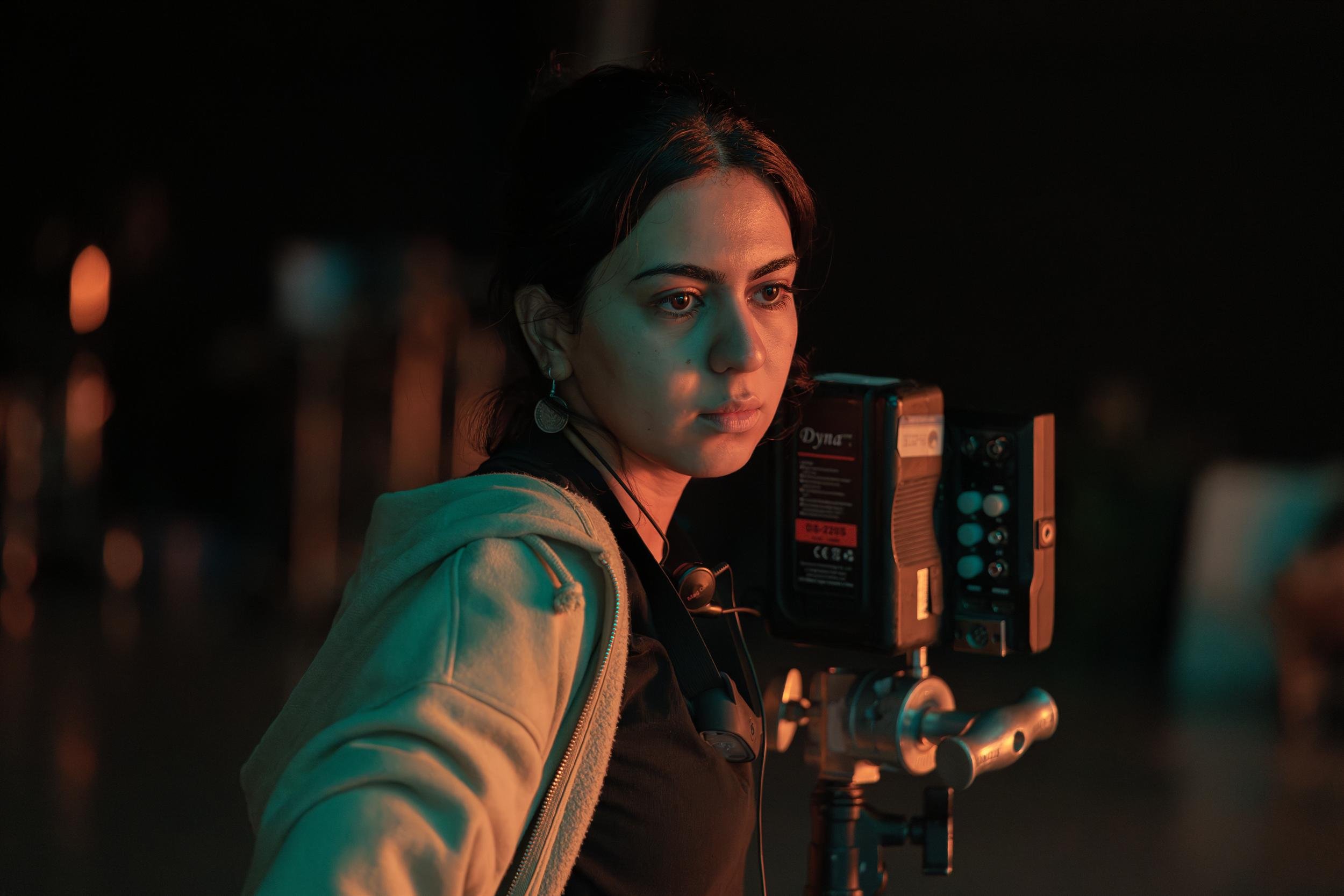 Ahlan Simsim unit still: a crew member in a beige hoodie stands beside production equipment under orange and teal light.