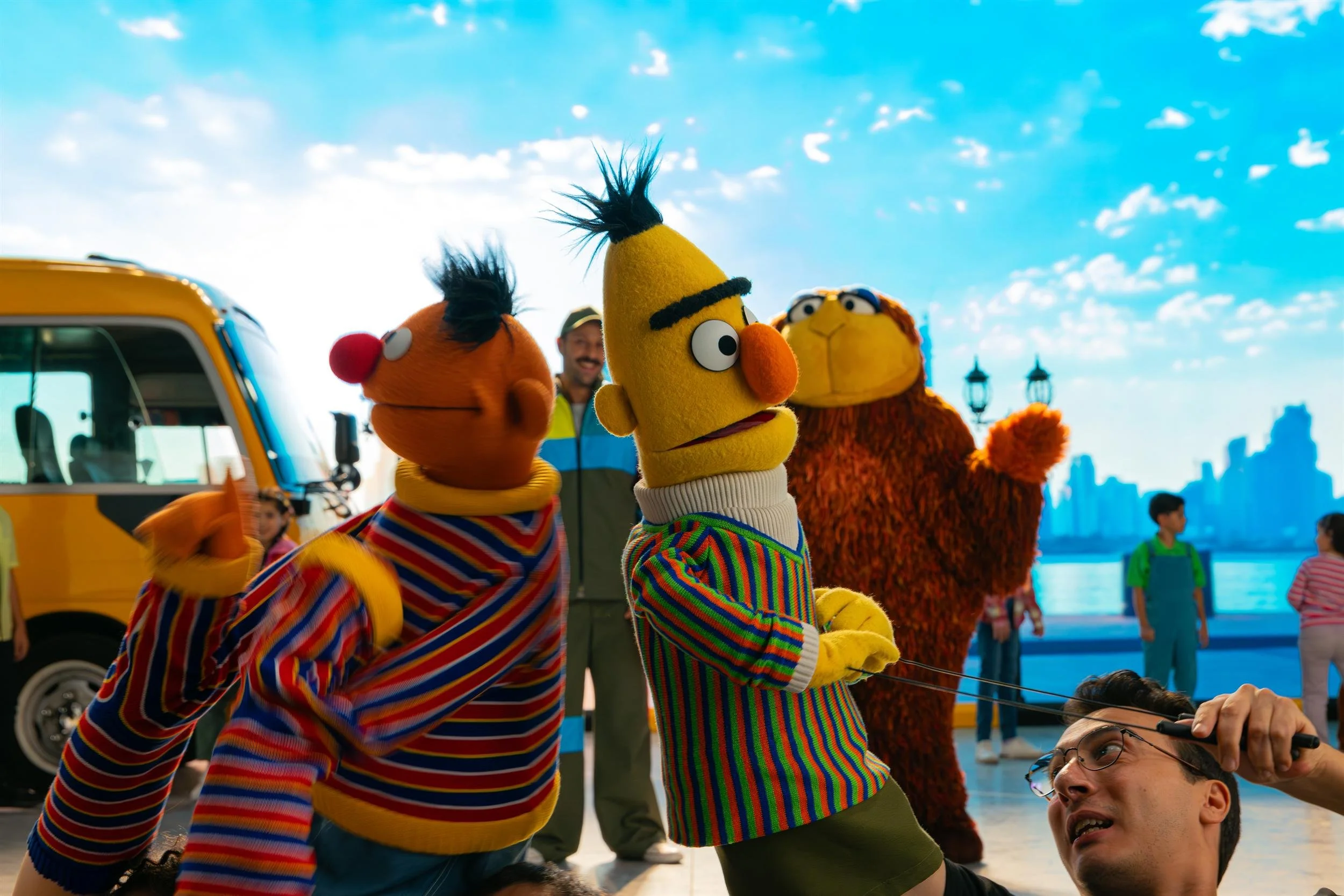 Ahlan Simsim unit still: Ernie, Bert, and a large brown Muppet on set with a puppeteer lying on the floor.