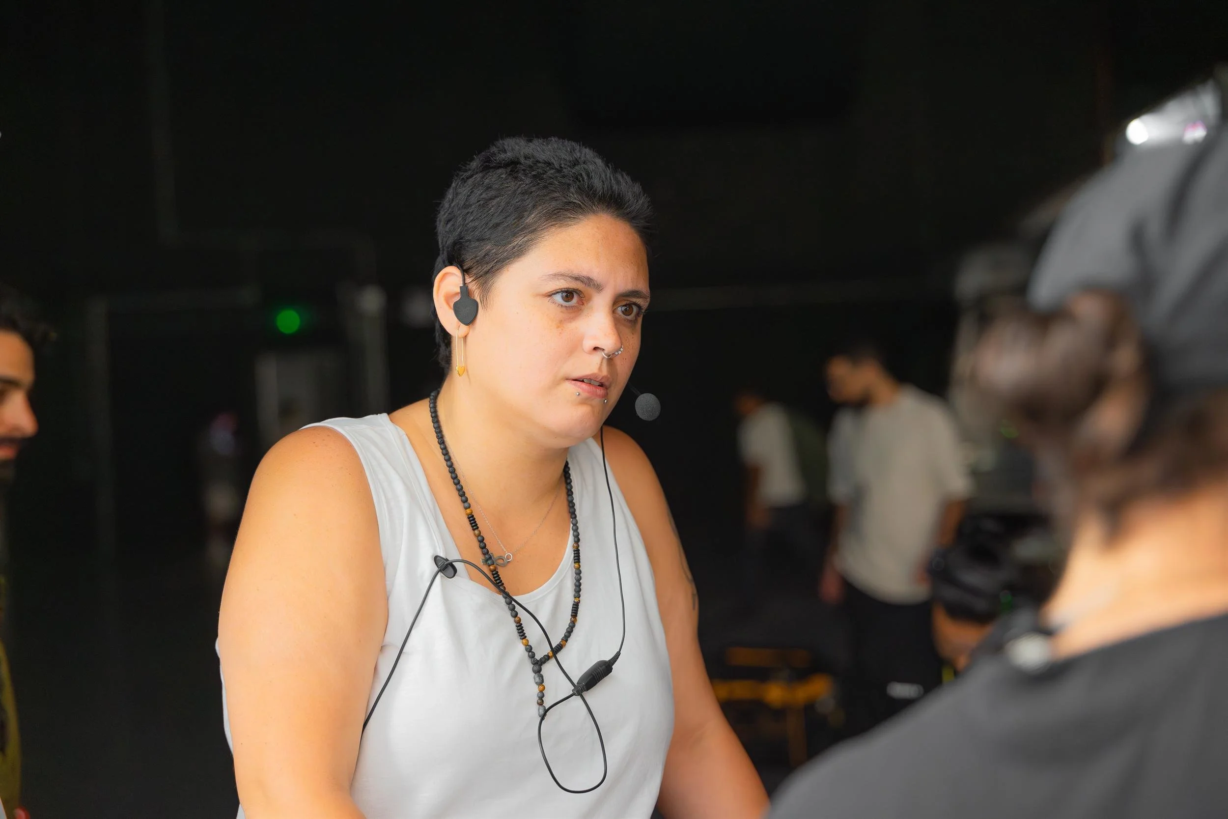 Ahlan Simsim unit still: A crew member wearing a headset and white tank top looks on from a dark studio set.