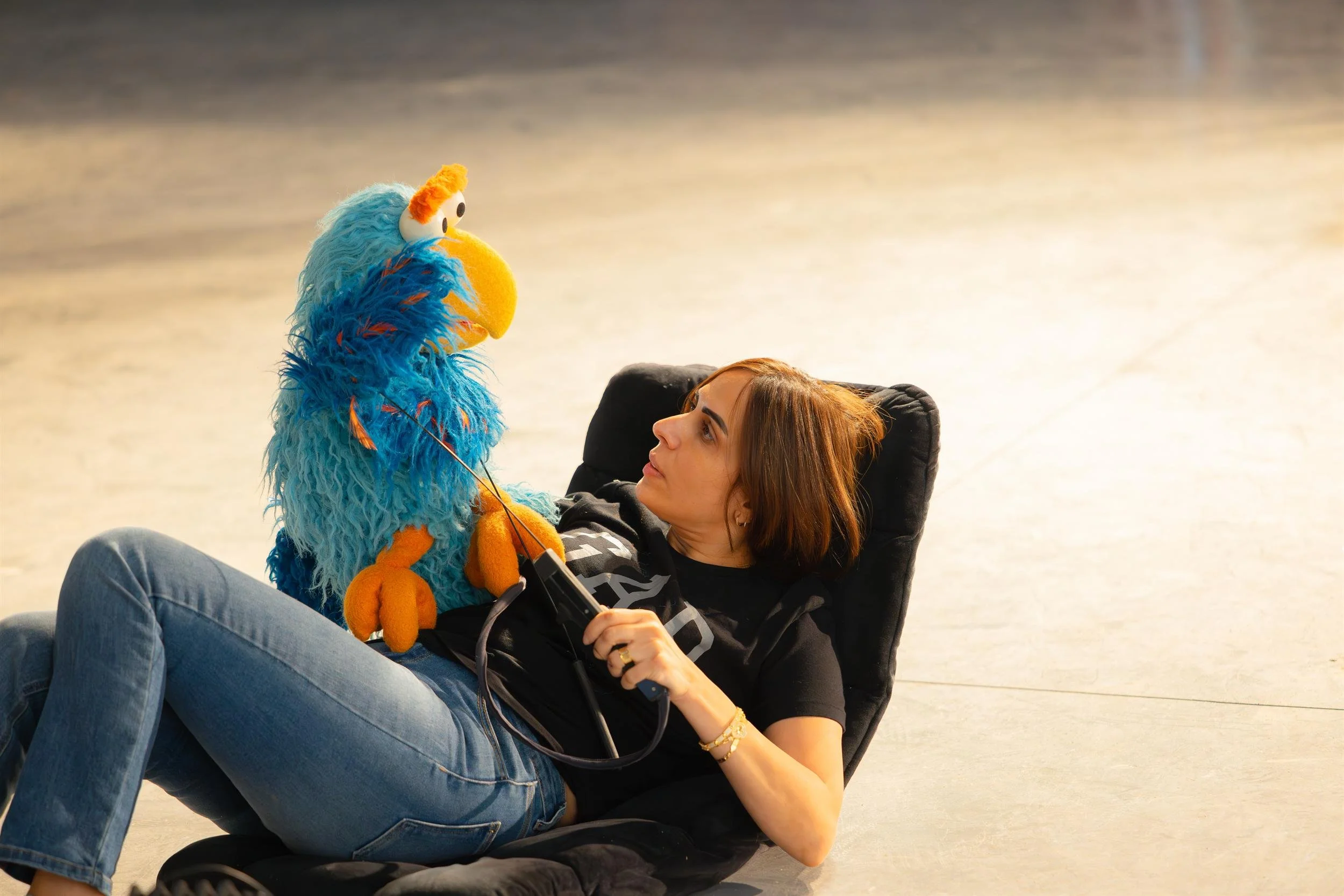 Ahlan Simsim unit still: a puppeteer lying on a floor mat holds a blue Muppet.
