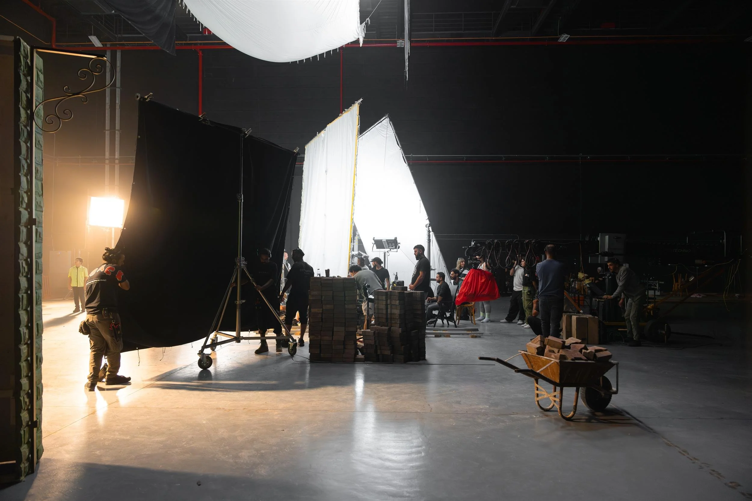 Ahlan Simsim unit still: Crew members work among lighting screens, brick stacks, and a wooden wheelbarrow in a large studio.