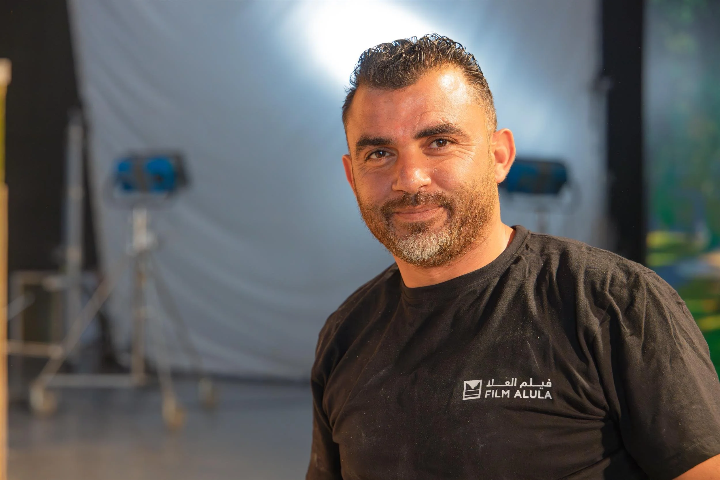 Ahlan Simsim unit still: A smiling crew member in a black t-shirt poses in a studio with lights behind him.