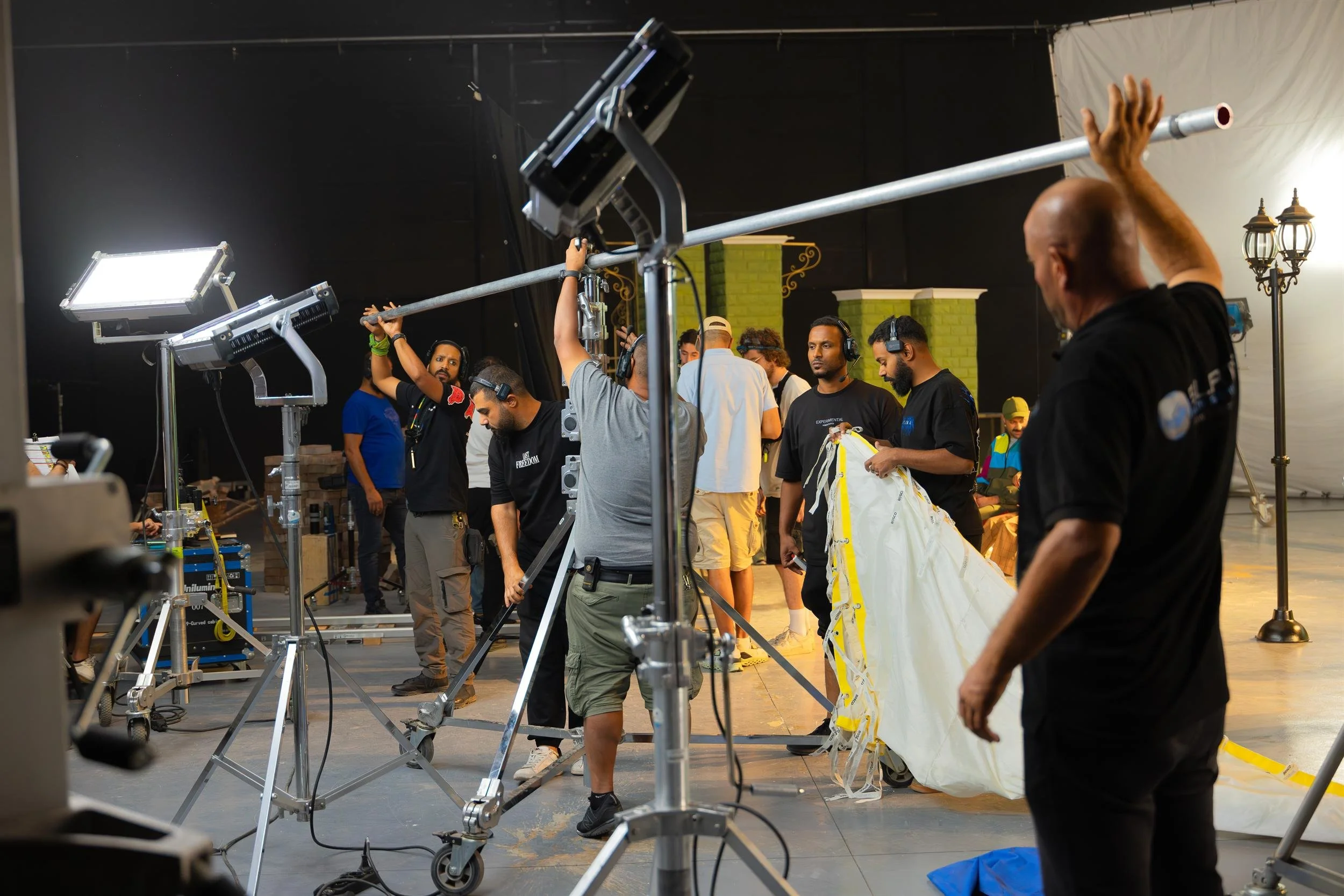 Ahlan Simsim unit still: Crew members set up lighting, a boom pole, and a large white diffusion sheet in a studio.