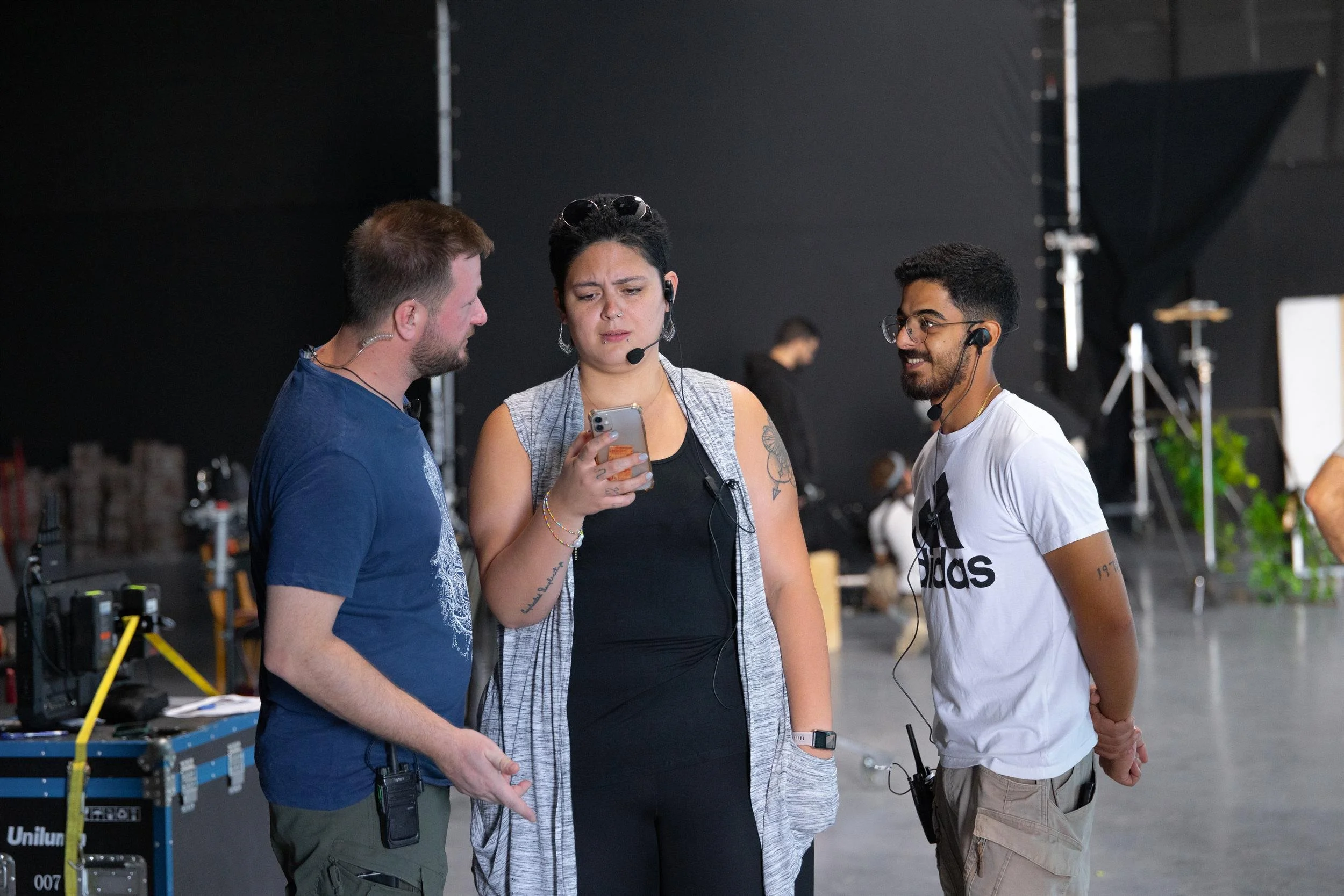 Ahlan Simsim unit still: three crew members in headsets gather around a smartphone in the studio.