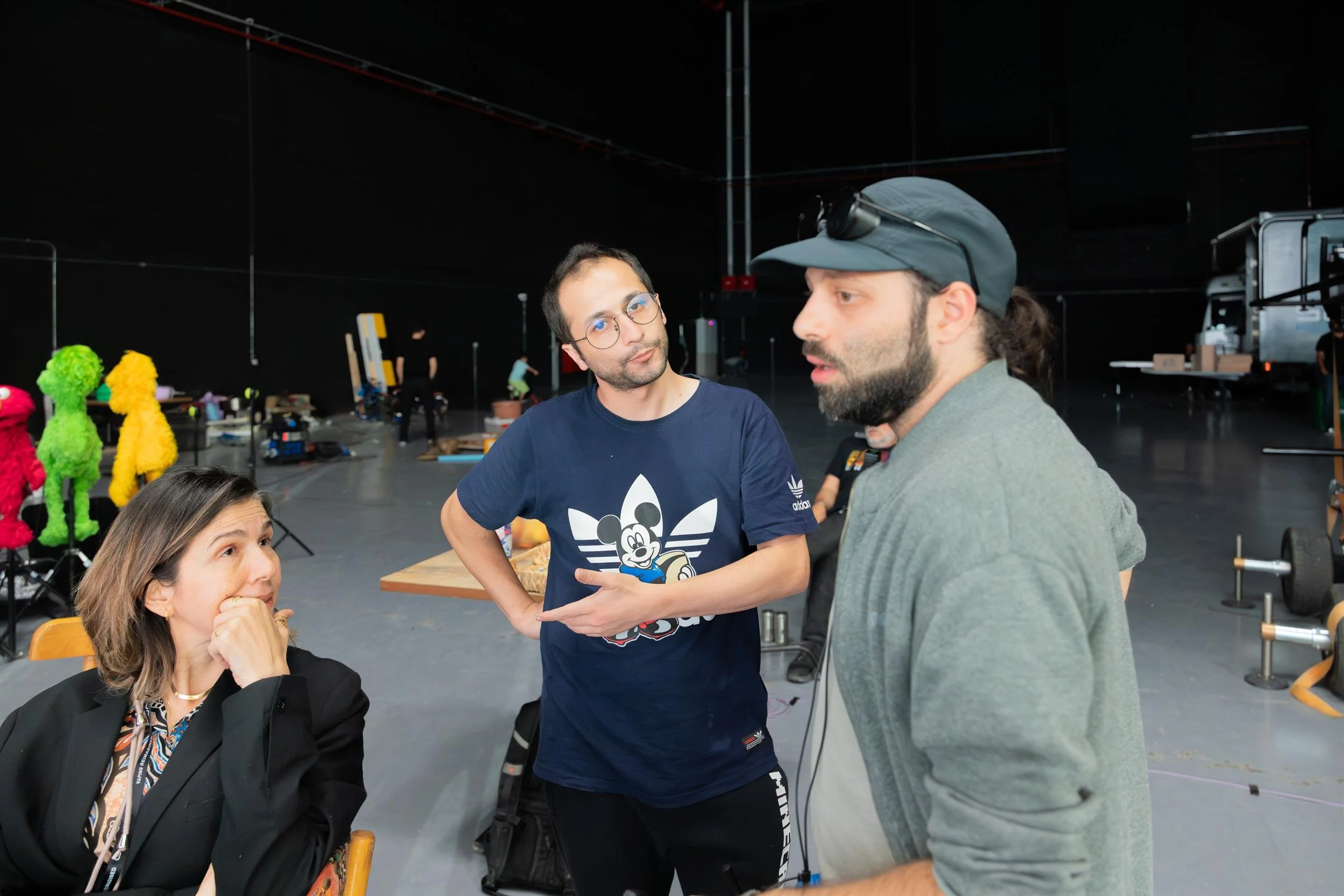 Ahlan Simsim unit still: crew members talk on a studio floor with Elmo and other Muppets on stands behind them.