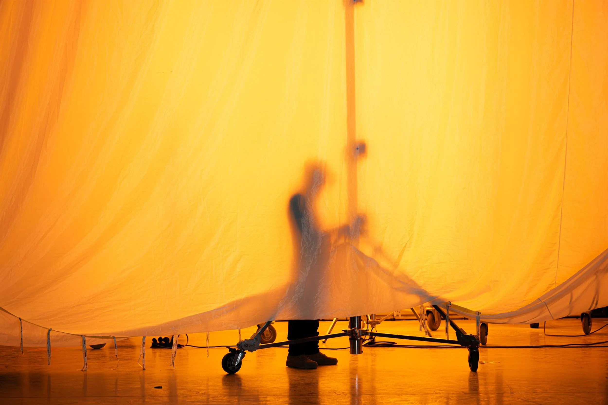 Ahlan Simsim unit still: a crew member's silhouette works behind a large glowing orange fabric sheet.