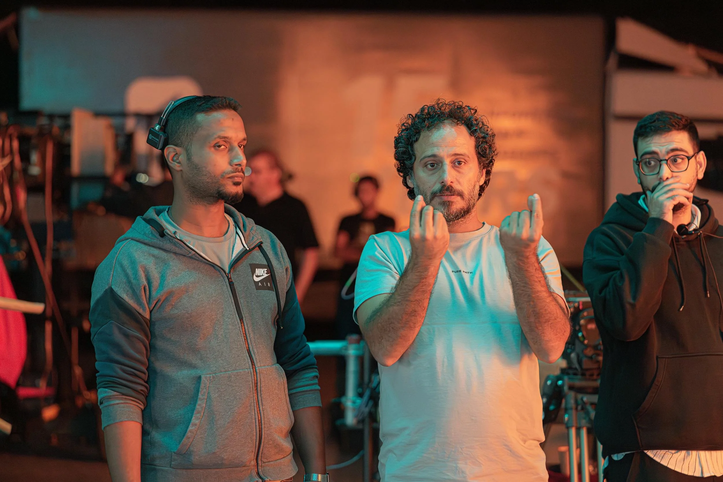 Ahlan Simsim unit still: three crew members confer on a dimly lit set with warm orange lights.