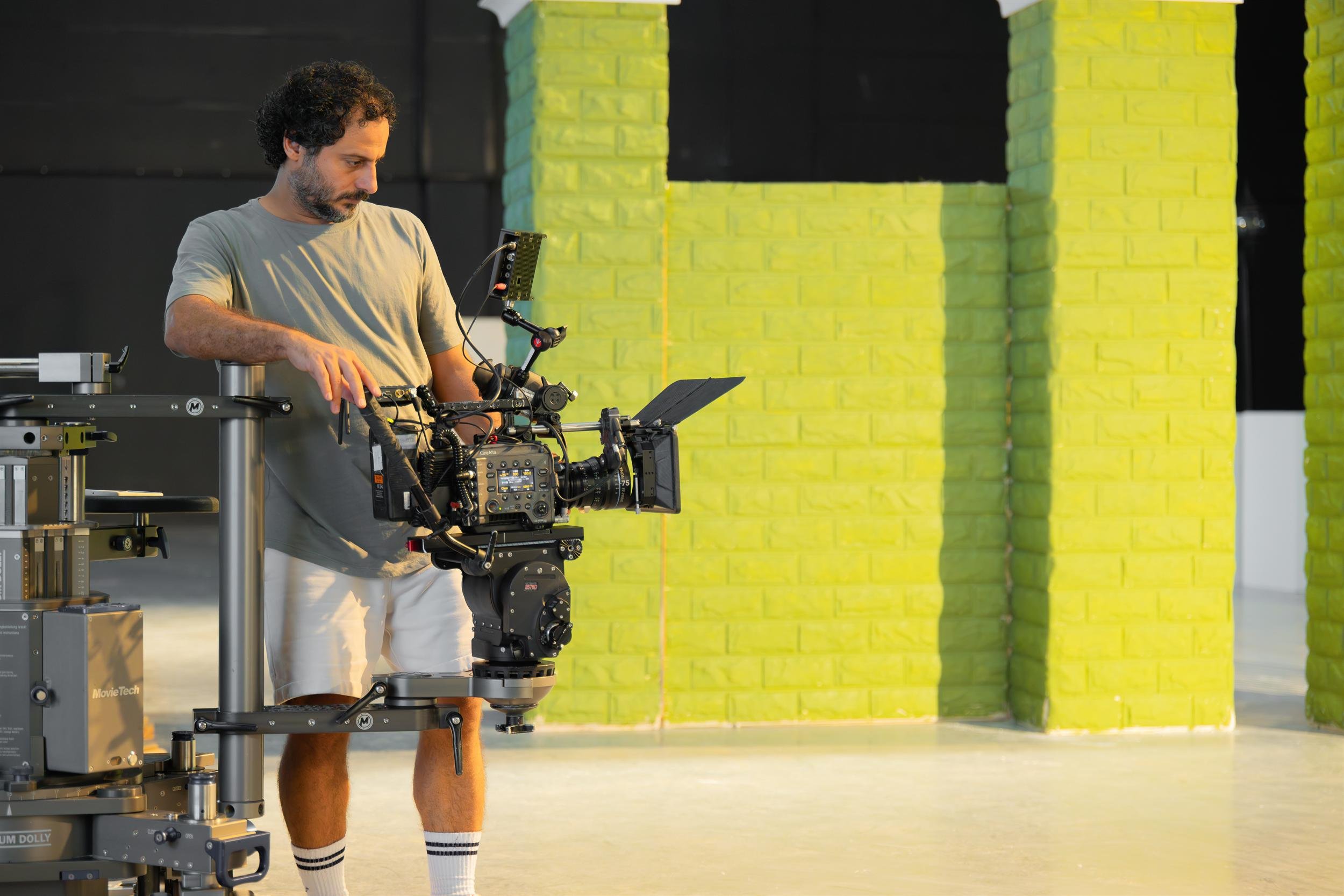 Ahlan Simsim unit still: A crew member leans over a cinema camera mounted on a dolly beside green brick set pieces.
