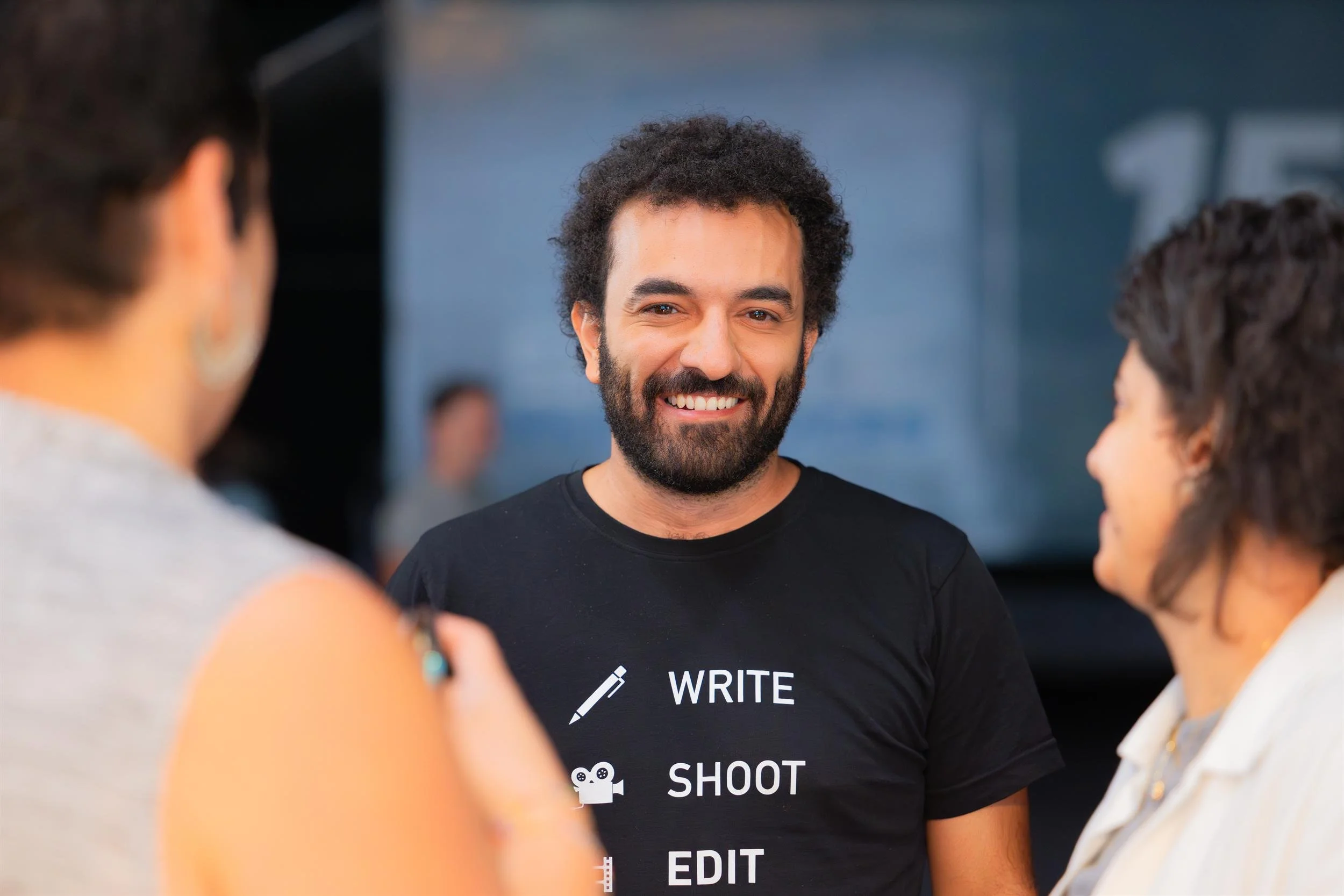Ahlan Simsim unit still: a smiling crew member in a WRITE SHOOT EDIT t-shirt talks with colleagues on set.