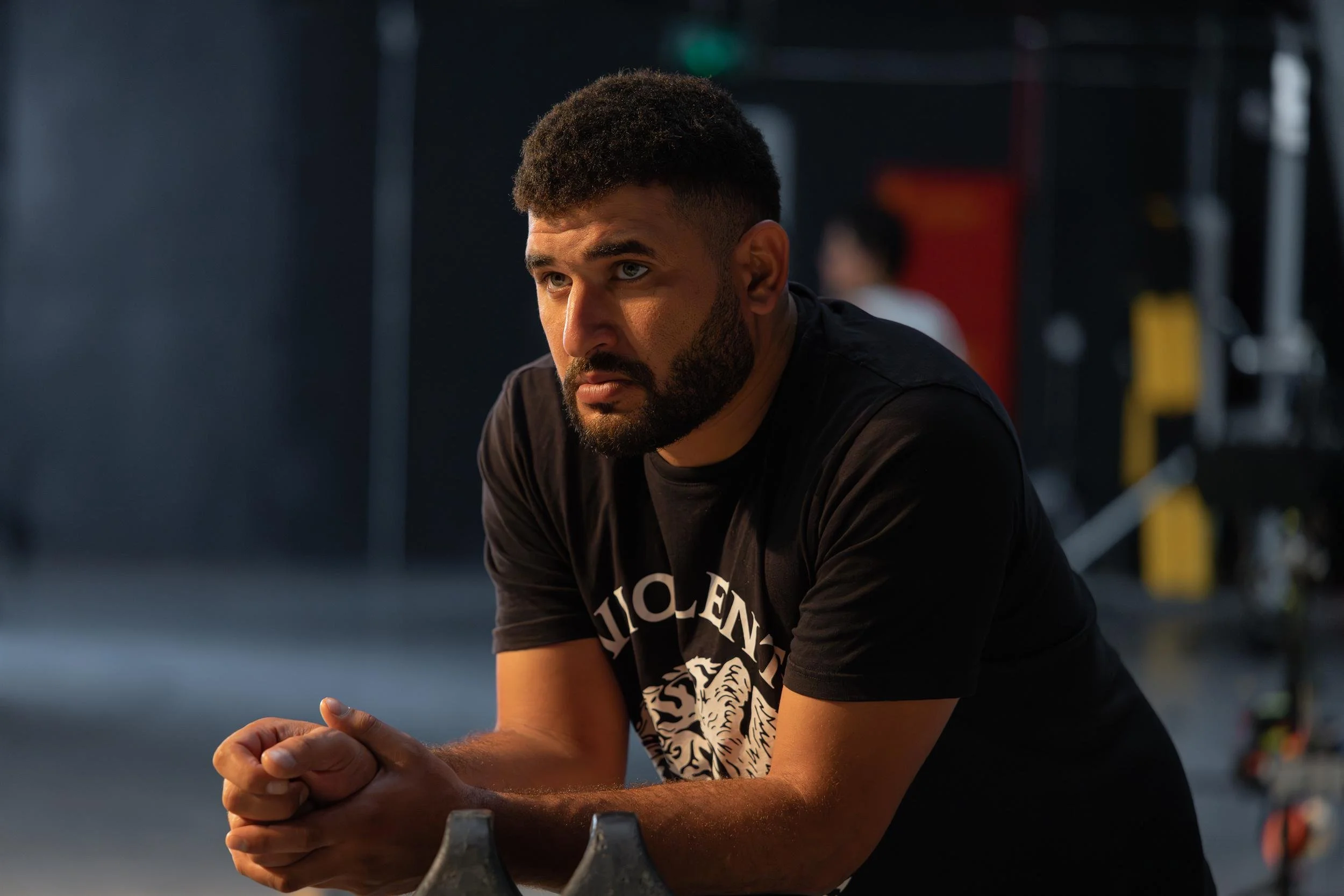 Ahlan Simsim unit still: A bearded man in a black t-shirt looks thoughtfully off-camera on a studio set.