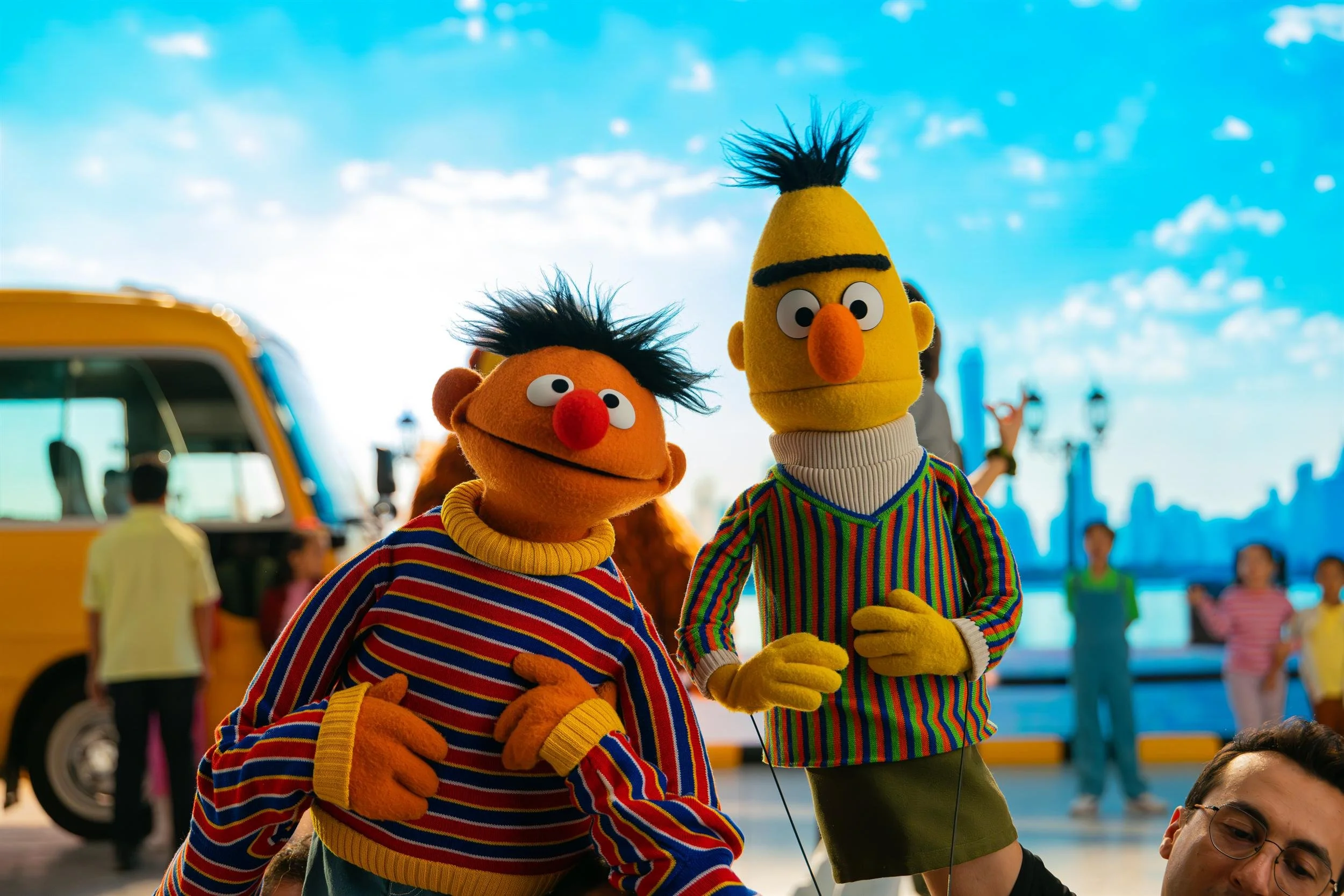 Ahlan Simsim unit still: Ernie and Bert stand side by side in front of a yellow bus and LED city skyline.