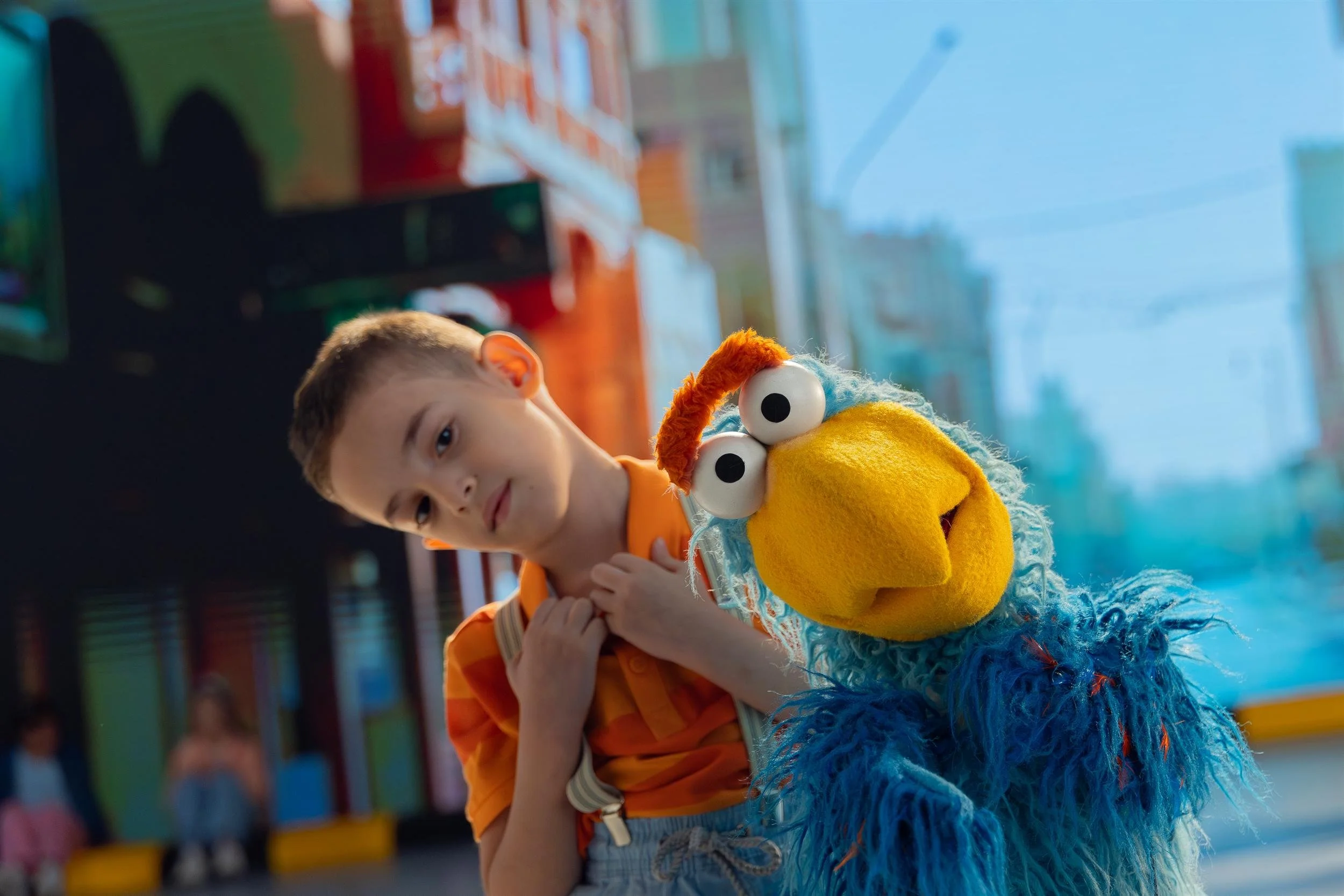 Ahlan Simsim key art: a boy leans in beside the blue and yellow bird muppet on the street set.
