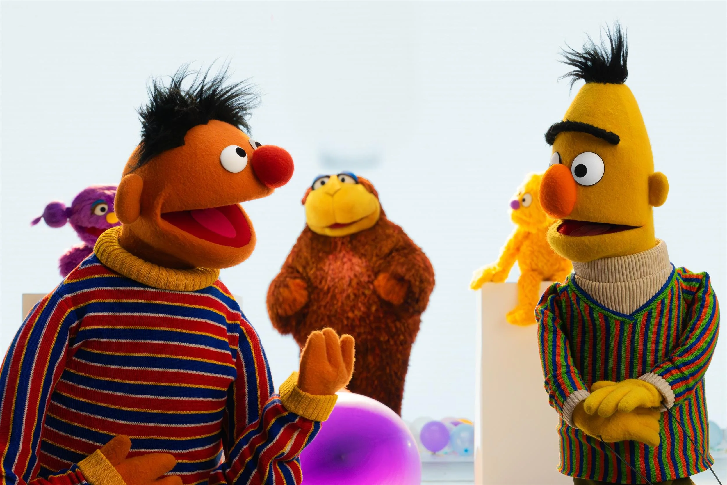Ahlan Simsim key art: Ernie and Bert talk in a bright studio with a brown Muppet and other friends behind them.