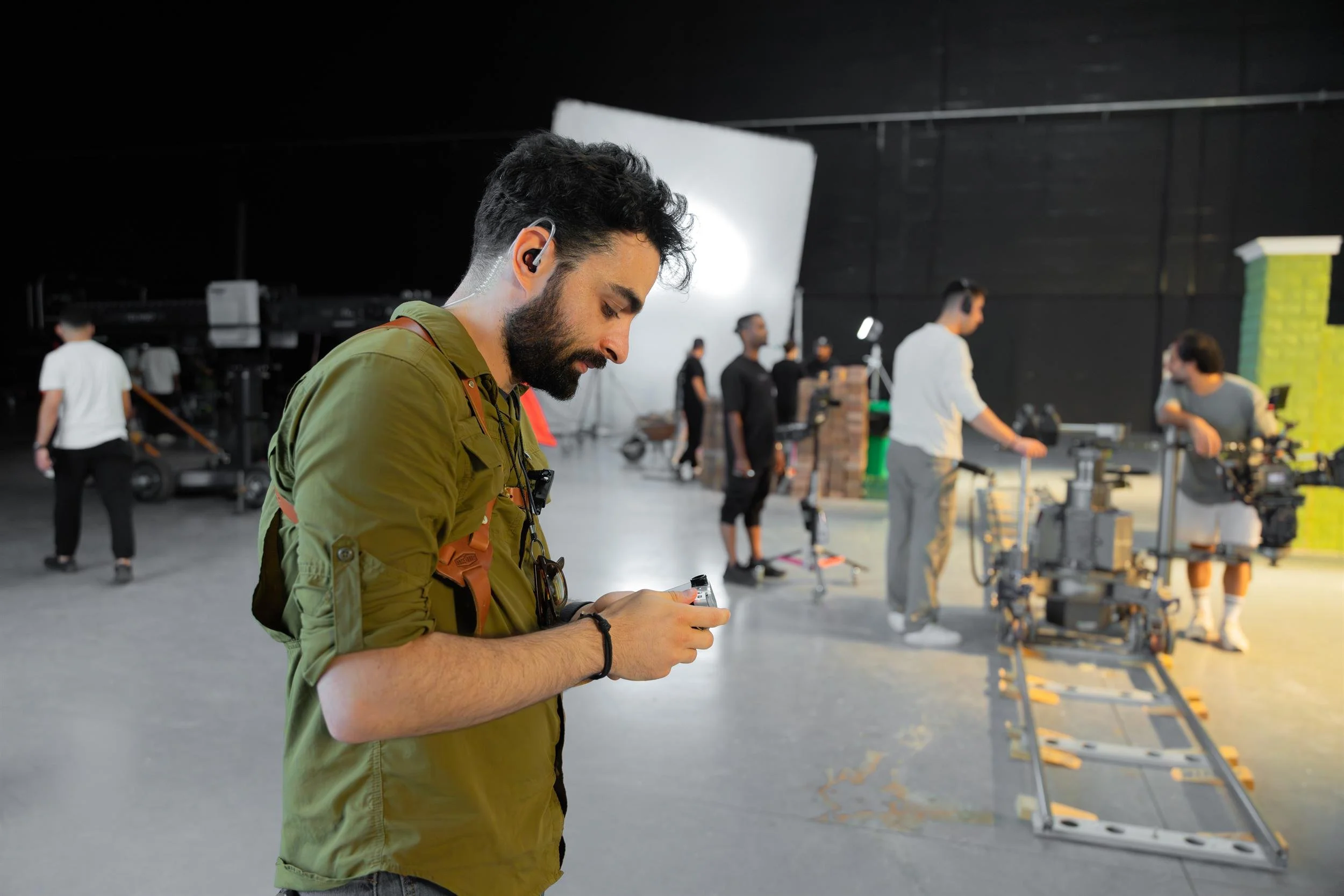 Ahlan Simsim unit still: A crew member checks a handheld device while others work around a camera dolly on set.