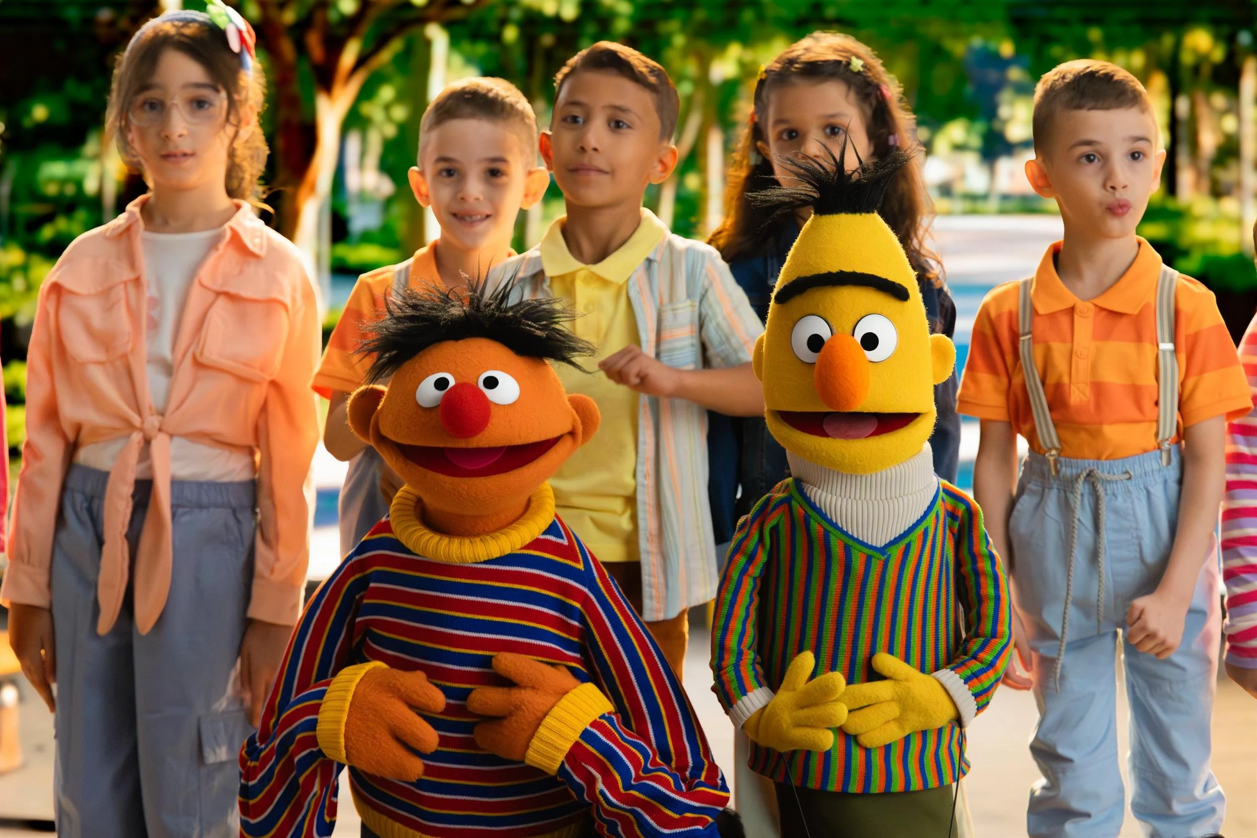 Ahlan Simsim key art: Ernie and Bert pose with a group of smiling children in a sunlit park.