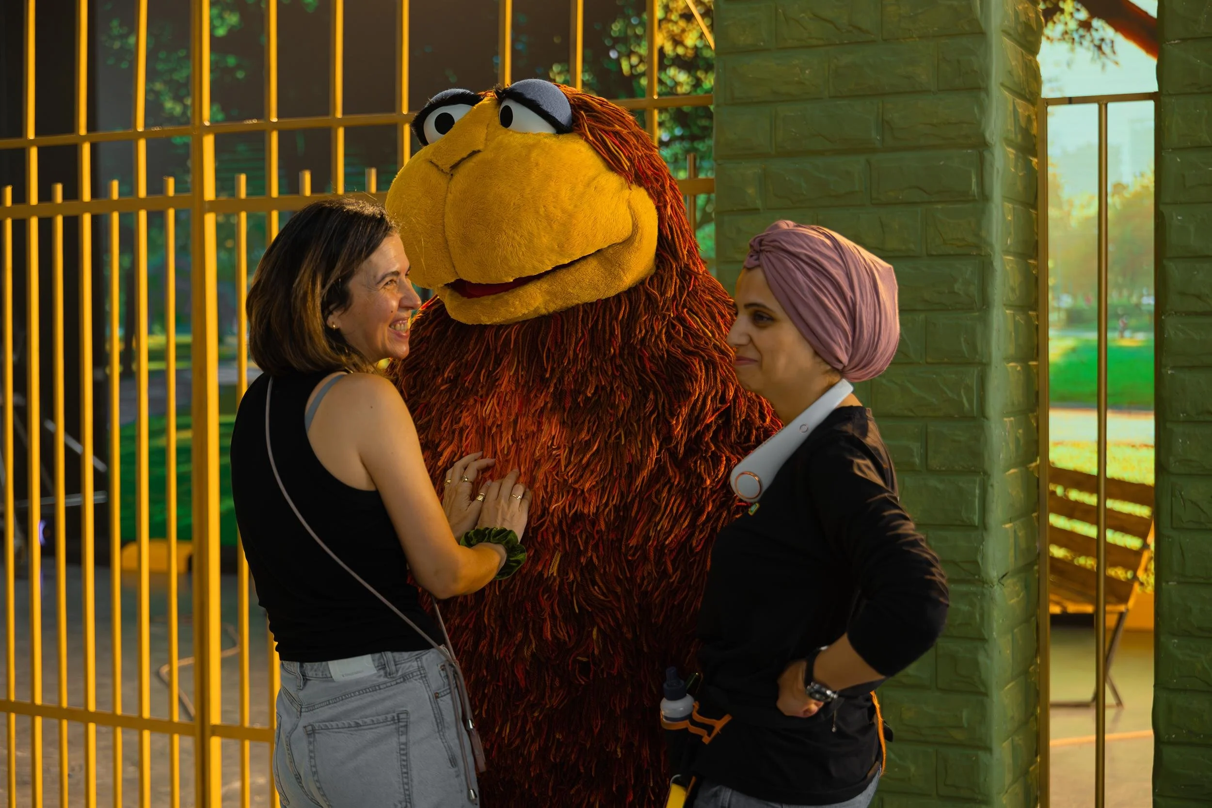 Ahlan Simsim unit still: Two crew members laugh with a large shaggy brown Muppet on a studio set.