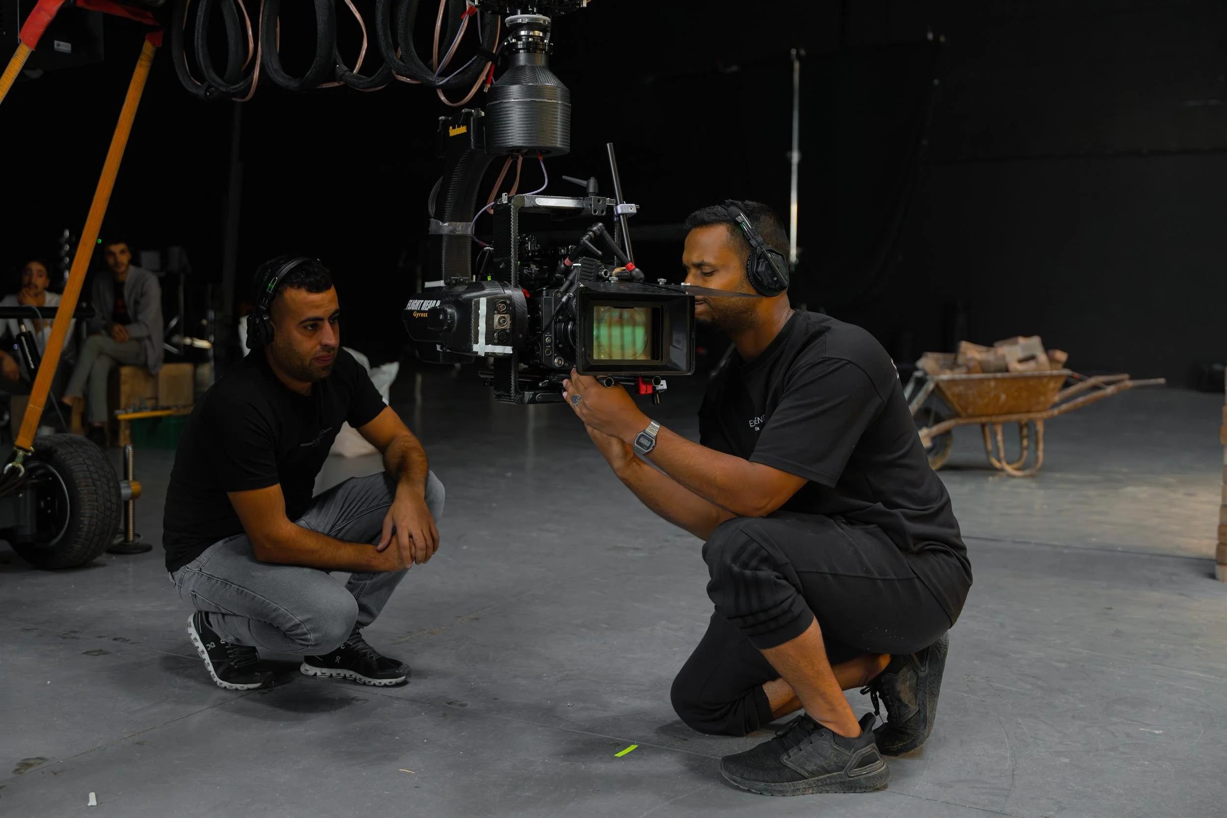 Ahlan Simsim unit still: Two crew members crouch in a studio to operate a large camera rig on a jib.