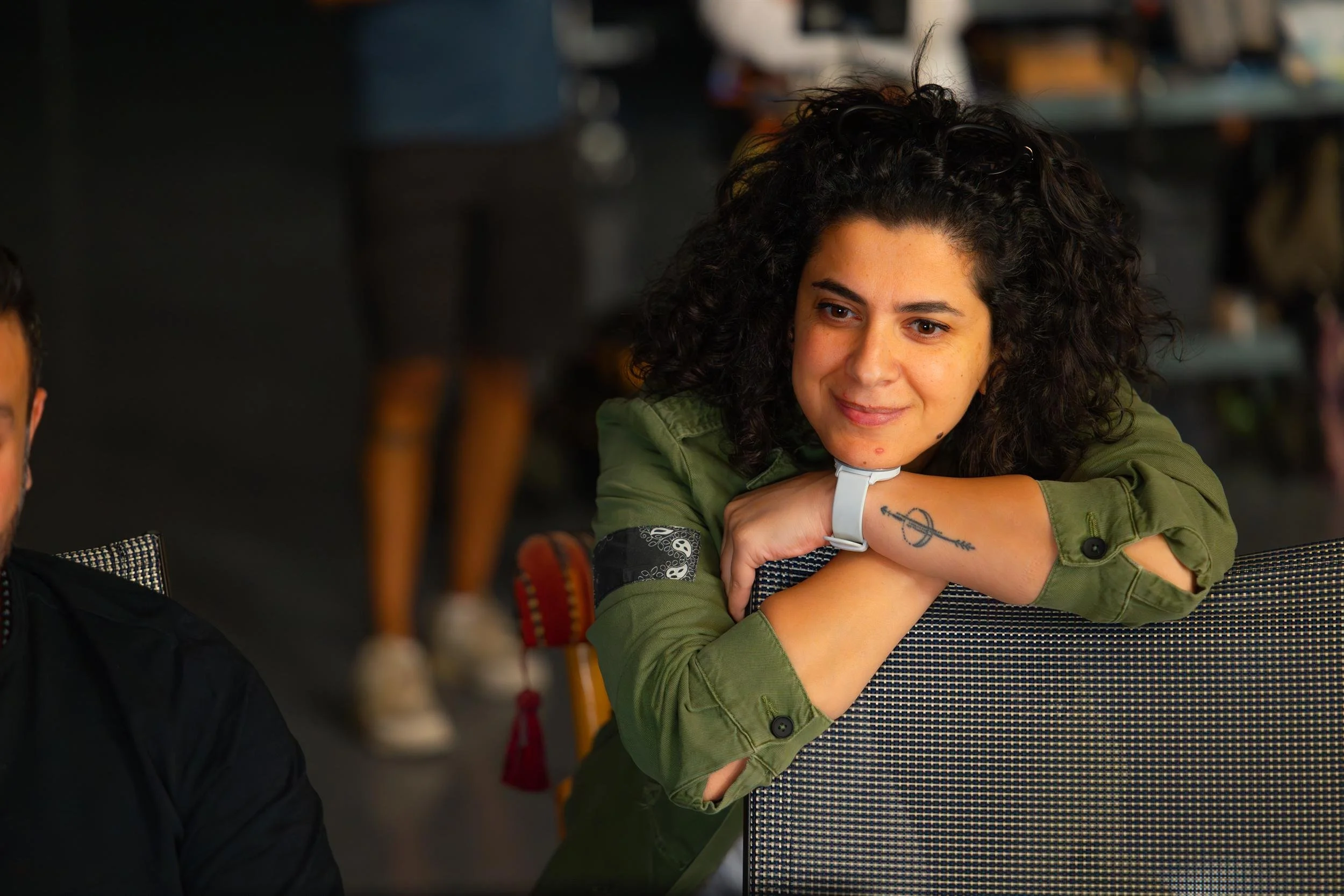 Ahlan Simsim unit still: a crew member with curly hair in a green jacket leans on a chair.
