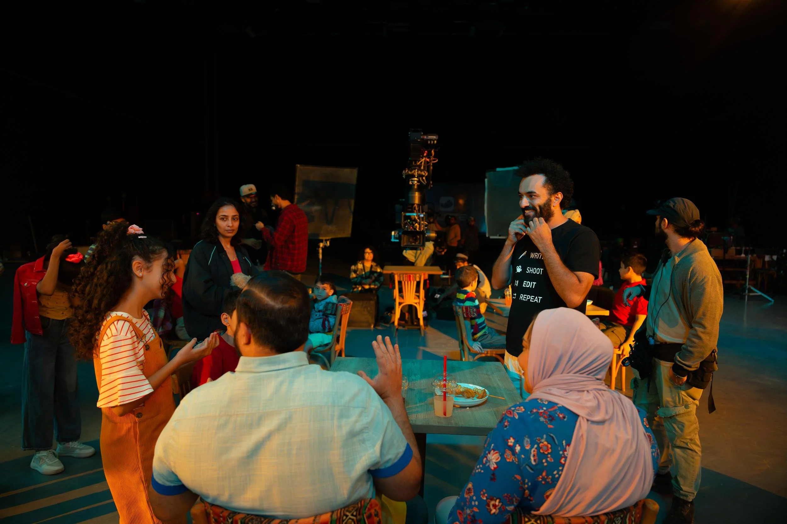 Ahlan Simsim unit still: crew and cast gather on a dark studio set with a camera crane in the background.