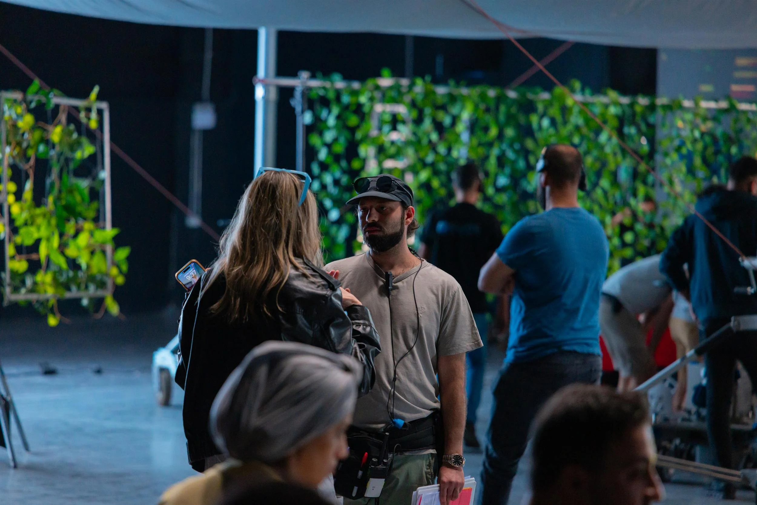 Ahlan Simsim unit still: a bearded crew member talks with a blonde colleague beside foliage backdrops.