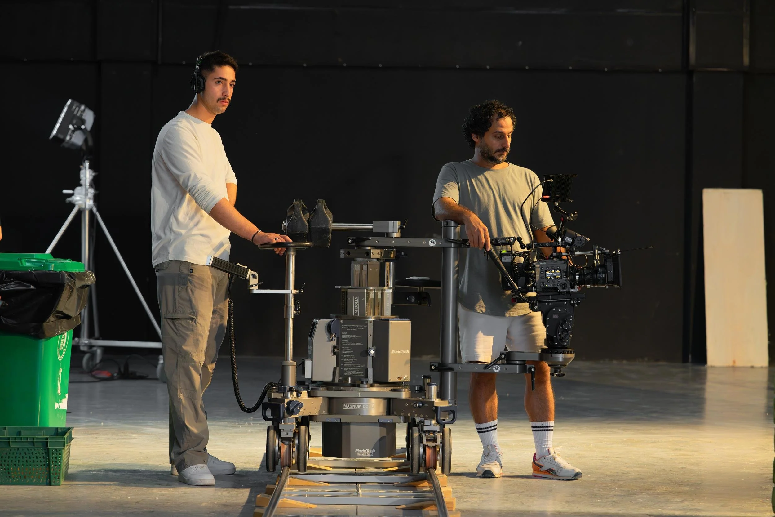 Ahlan Simsim unit still: Two crew members operate a camera on a large dolly on tracks in a dark studio.