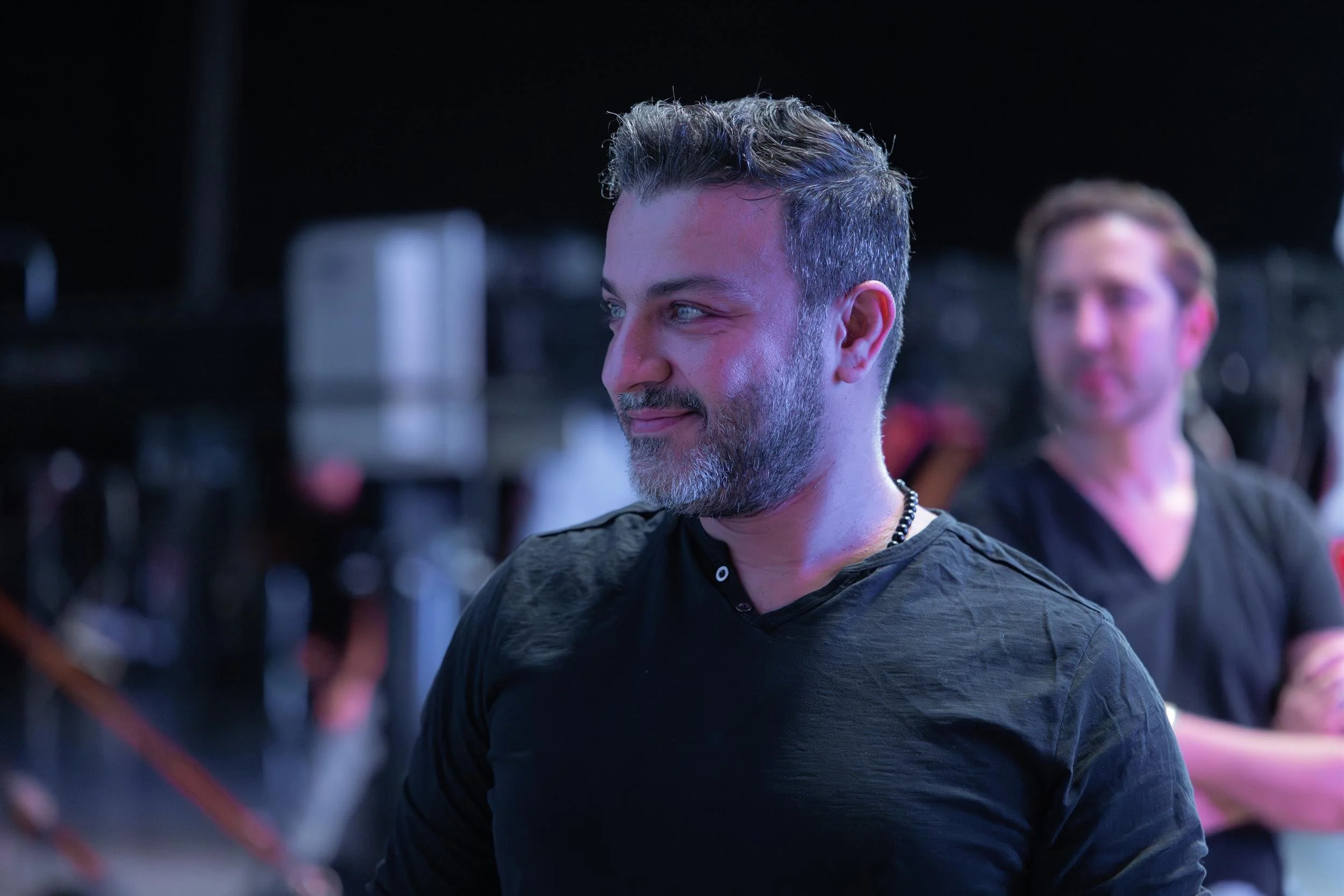 Ahlan Simsim unit still: A bearded crew member looks off-camera with a slight smile on a dark studio set.