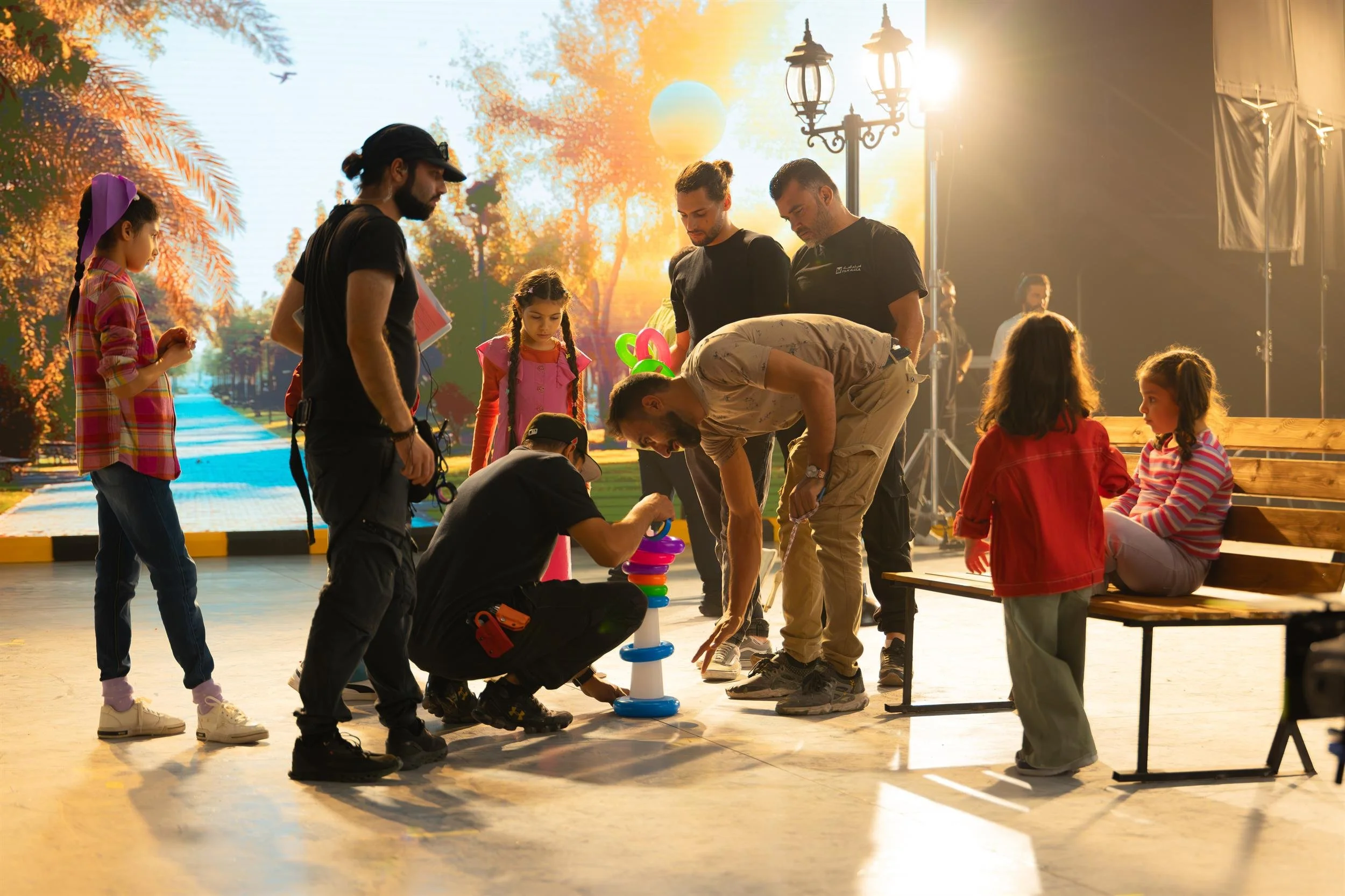 Ahlan Simsim unit still: crew members and children gather around a colorful ring stacker on a park set.