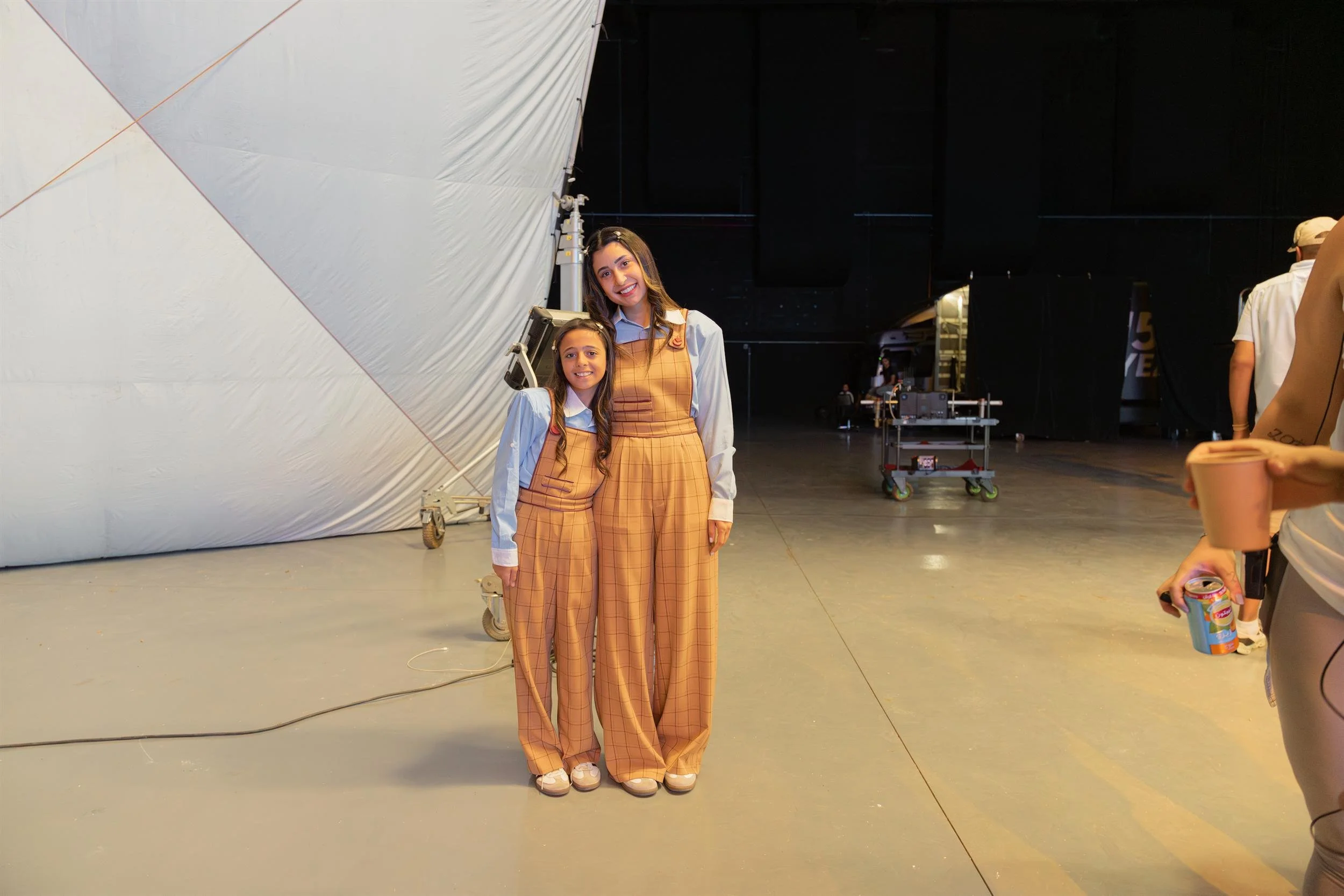 Ahlan Simsim unit still: A woman and a girl in matching plaid overalls and blue shirts pose together in a studio.