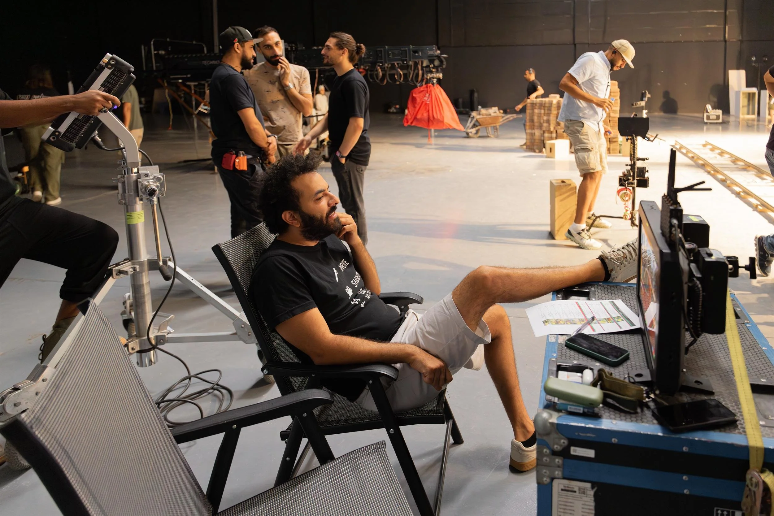 Ahlan Simsim unit still: A crew member watches a monitor with his feet on an equipment case in a large studio.