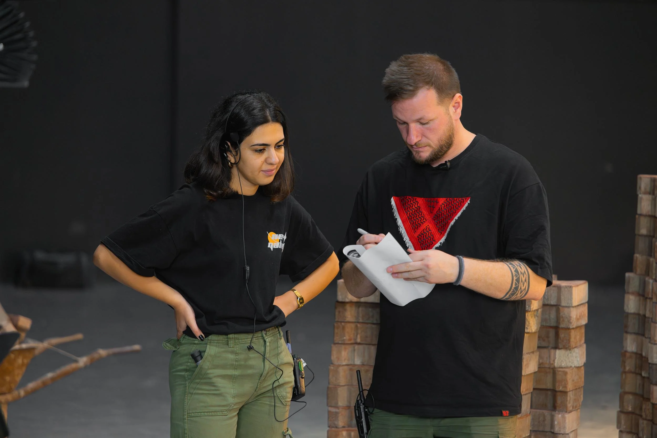 Ahlan Simsim unit still: Two crew members review notes beside stacks of bricks on a studio floor.