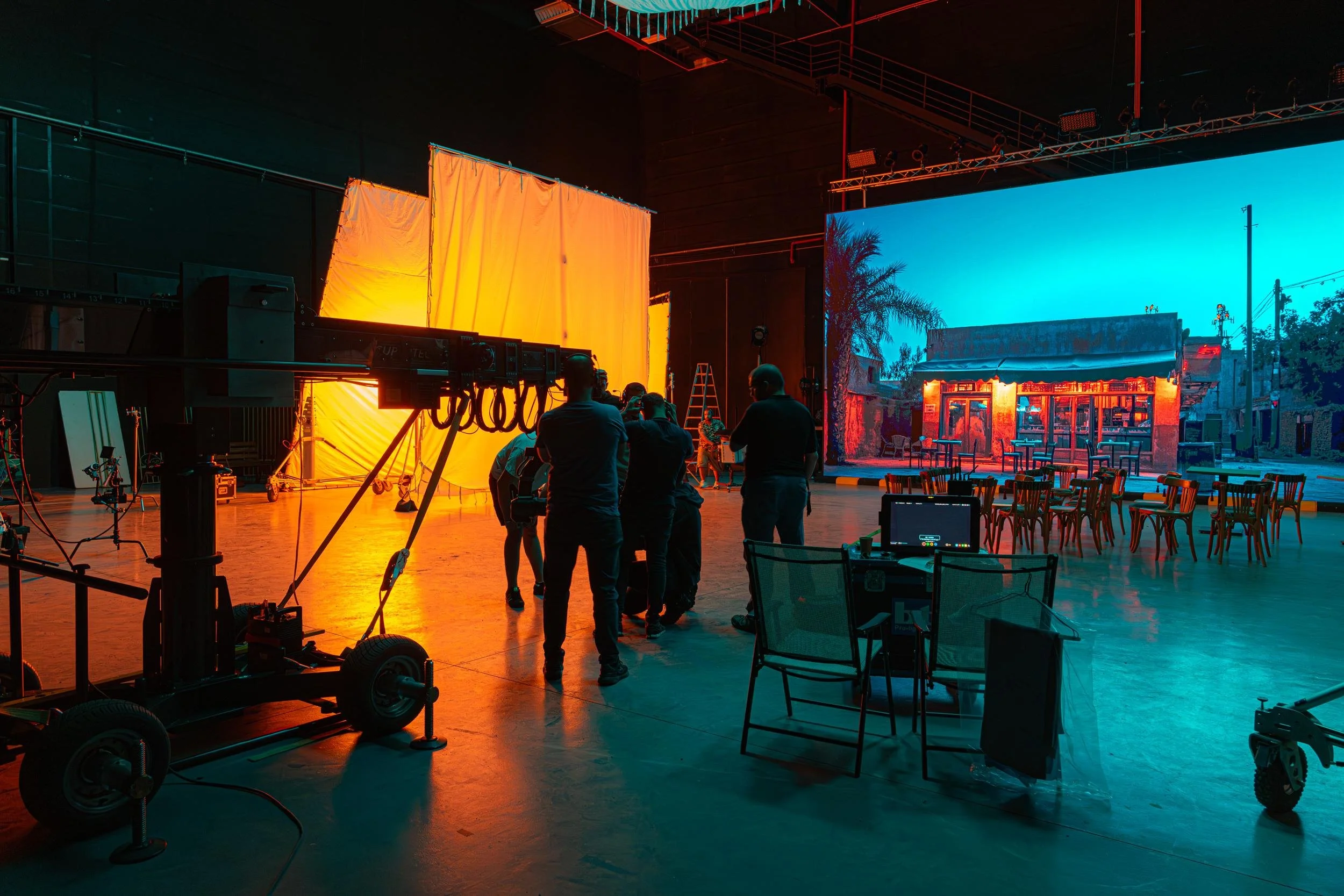 Ahlan Simsim unit still: orange light panels and an LED dusk street scene fill a dark studio with tables and chairs.
