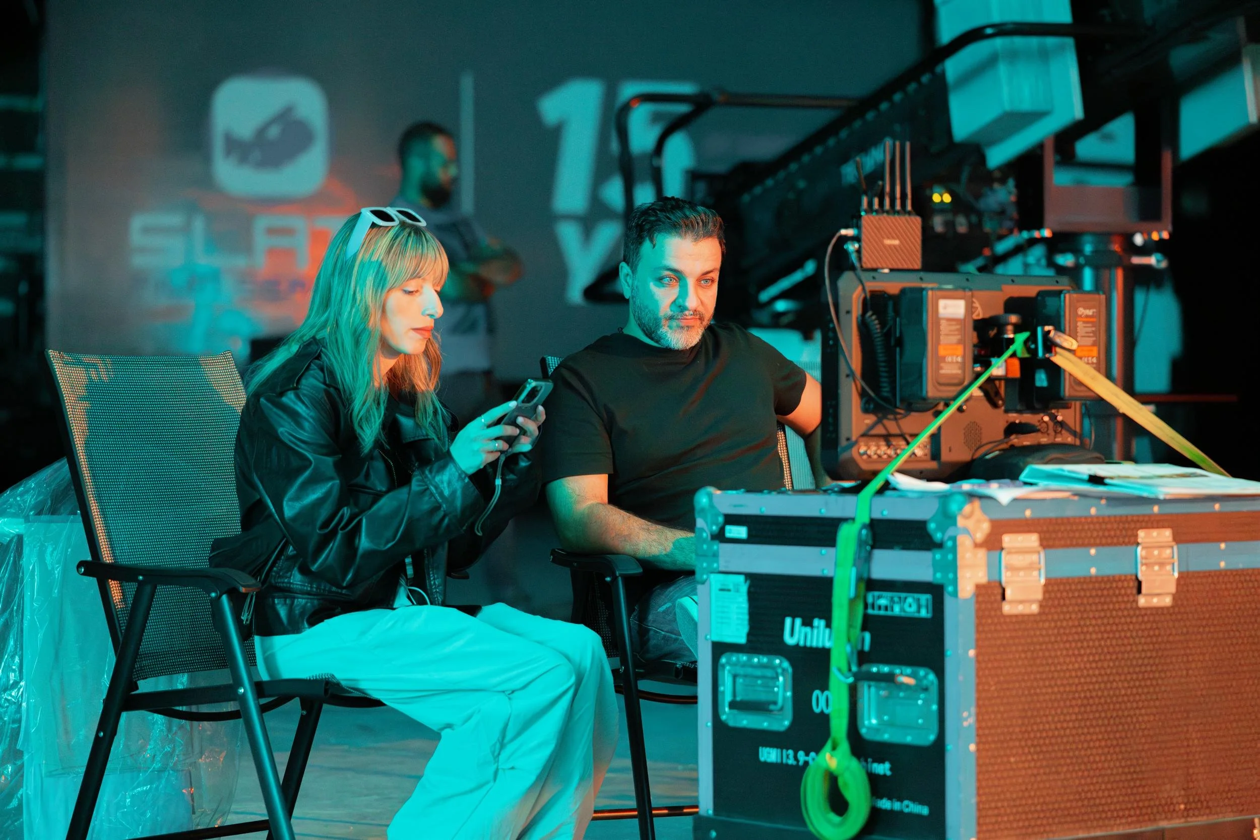 Ahlan Simsim unit still: two crew members sit behind a strapped production monitor on a dim set.