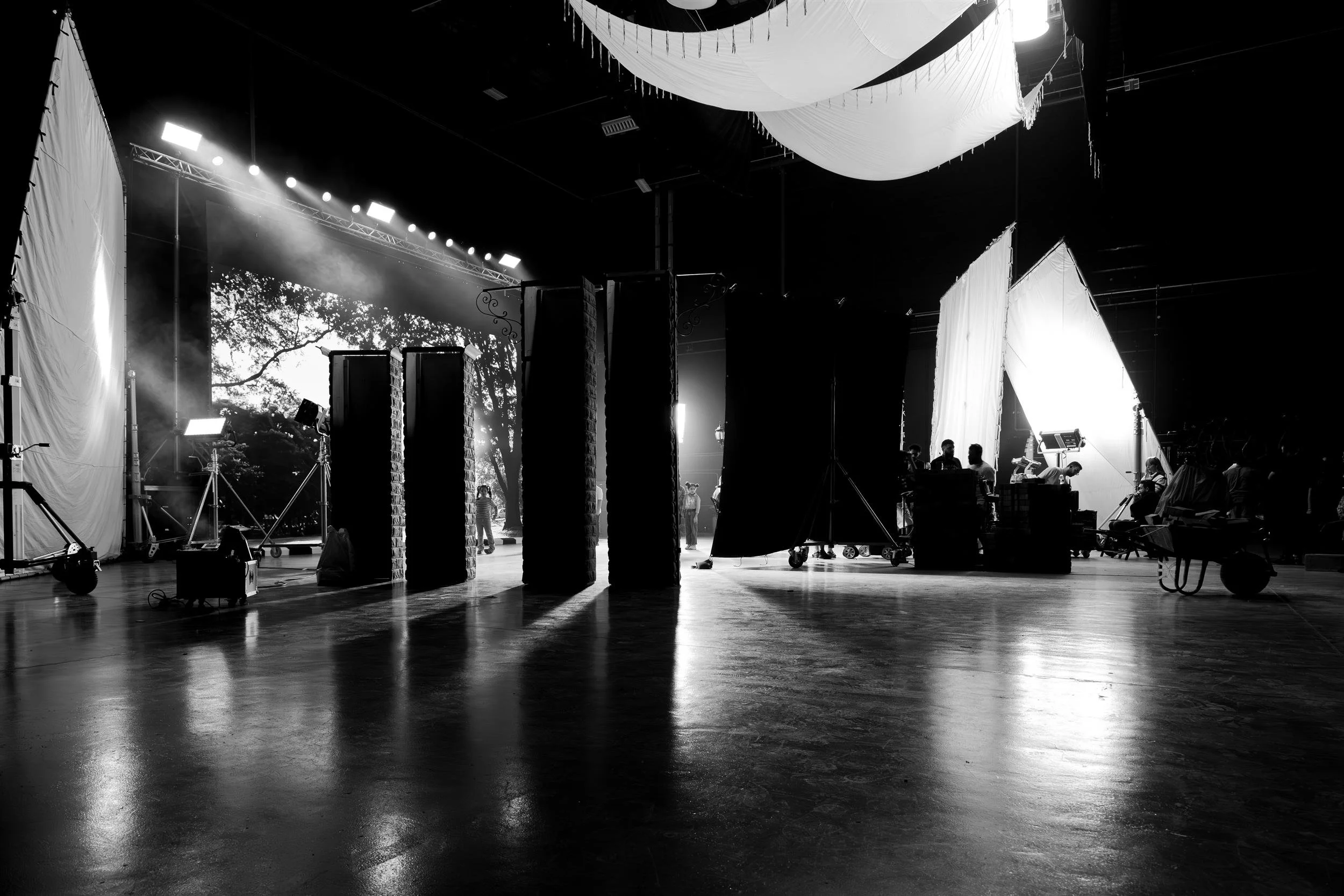 Ahlan Simsim unit still: A wide black-and-white view of the studio with lighting panels, crew, and tall set pieces.