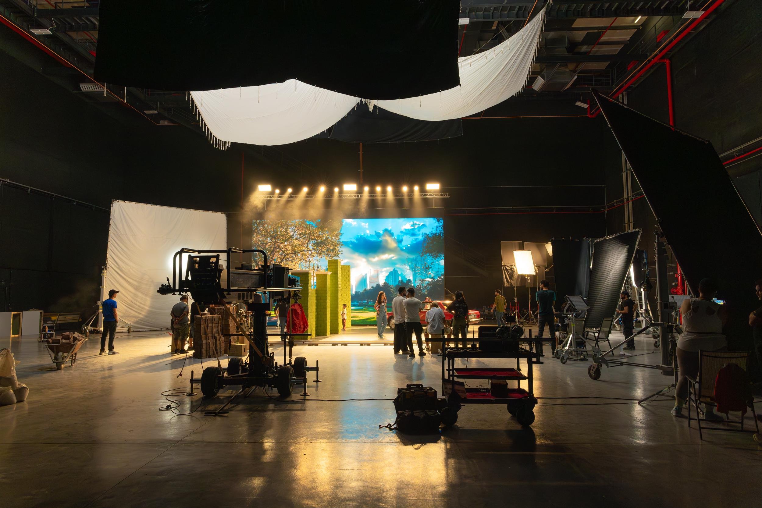 Ahlan Simsim unit still: Crew members work in a large studio around a lit set with a digital landscape backdrop.