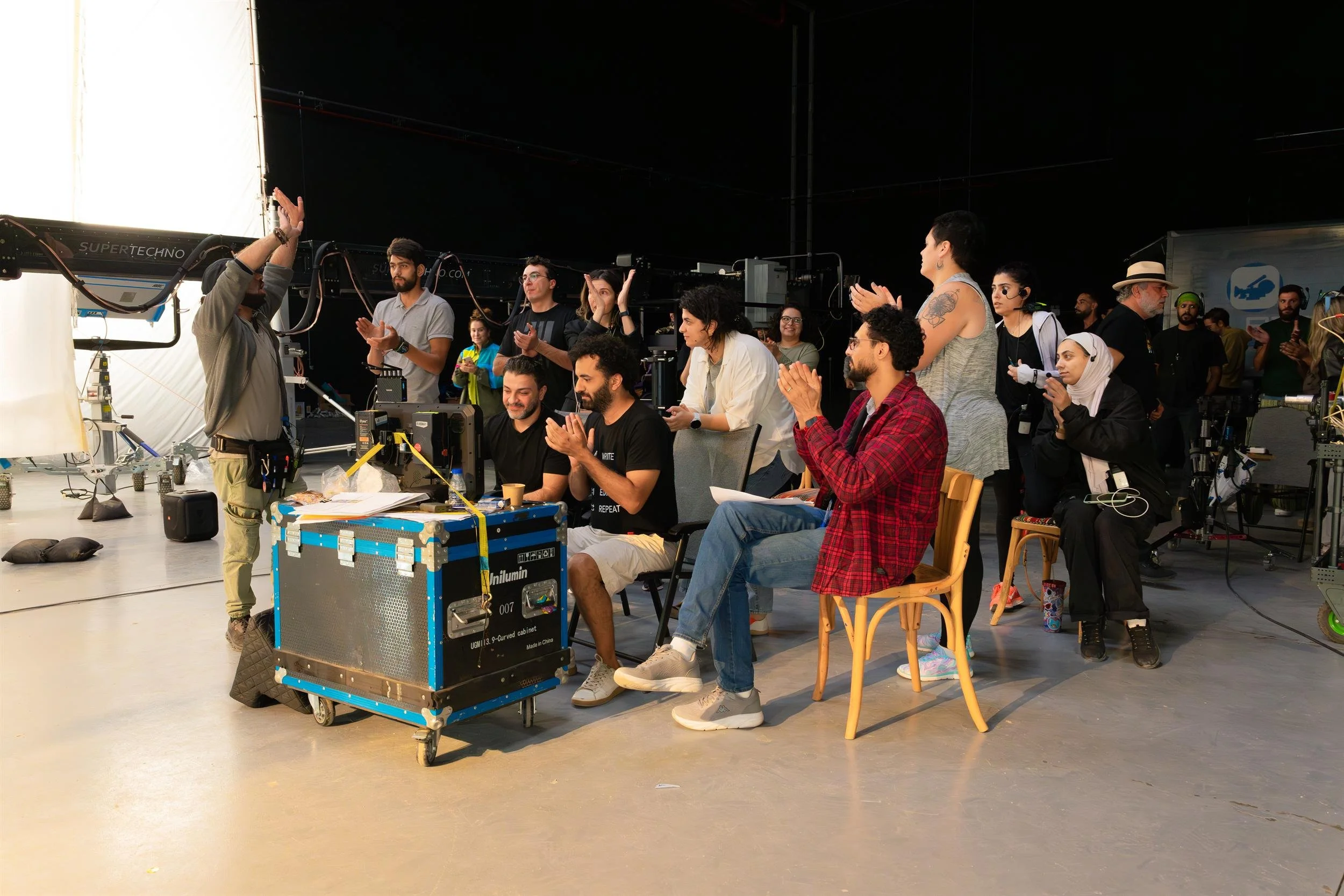 Ahlan Simsim unit still: a large group of crew members clap around production monitors in a studio.