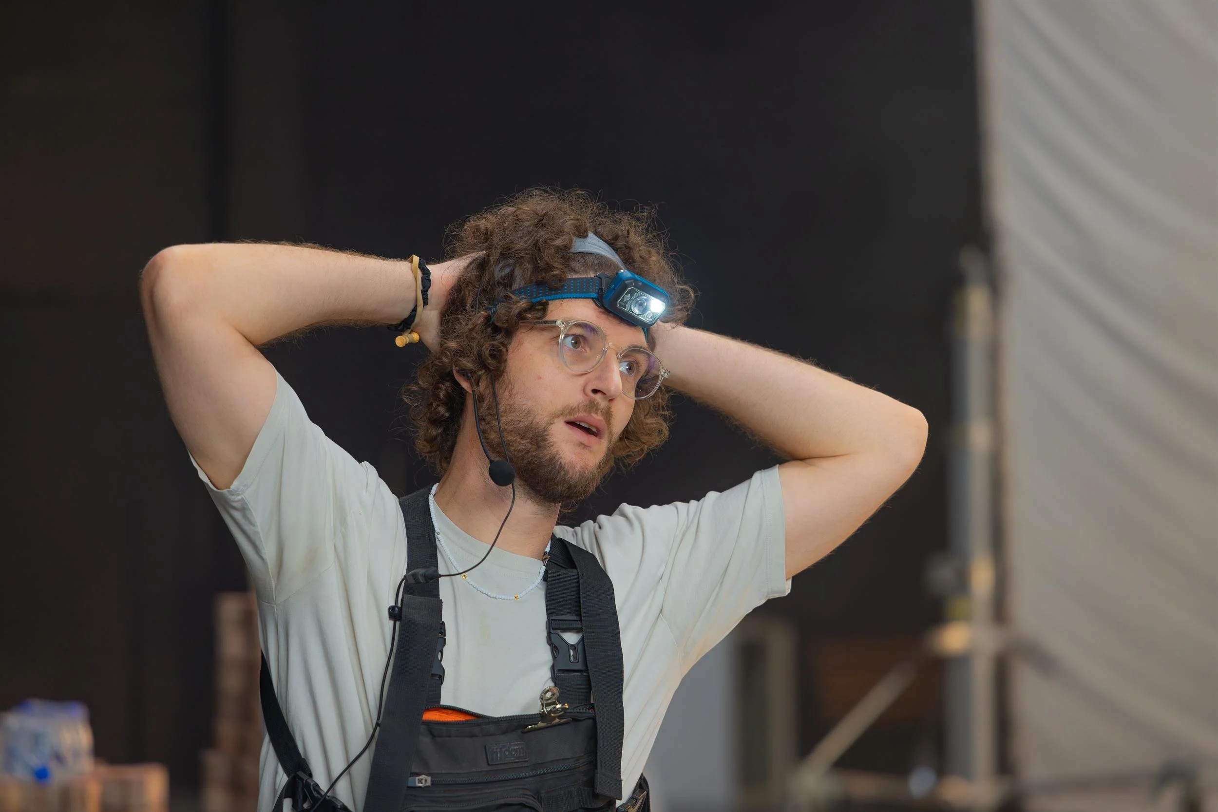 Ahlan Simsim unit still: A crew member with glasses and a lit headlamp clasps his hands behind his head on set.