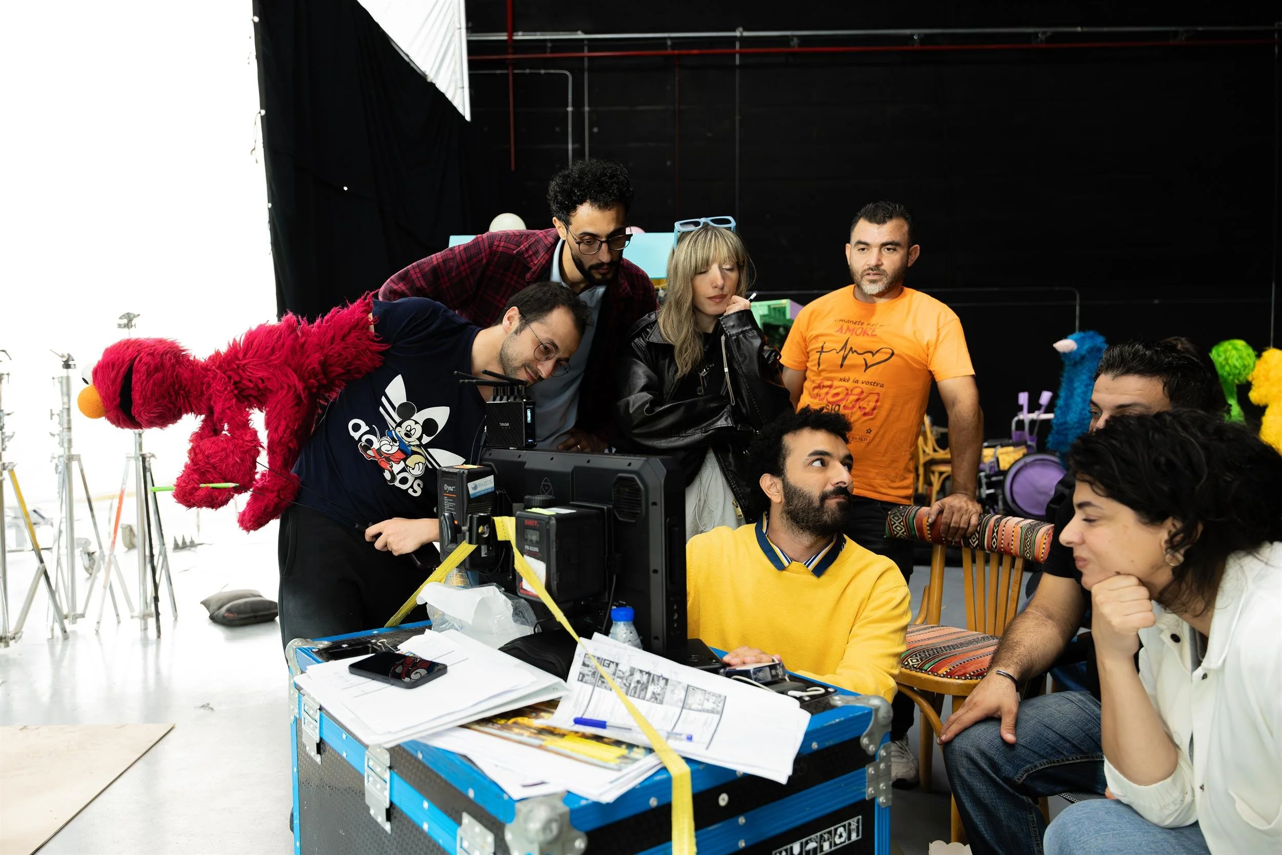 Ahlan Simsim unit still: crew gather around a monitor as a puppeteer holds Elmo toward the screen.