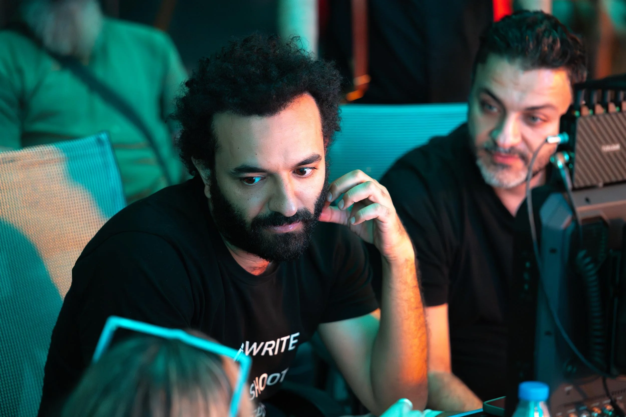 Ahlan Simsim unit still: two crew members sit in mesh chairs watching a monitor under teal and orange light.
