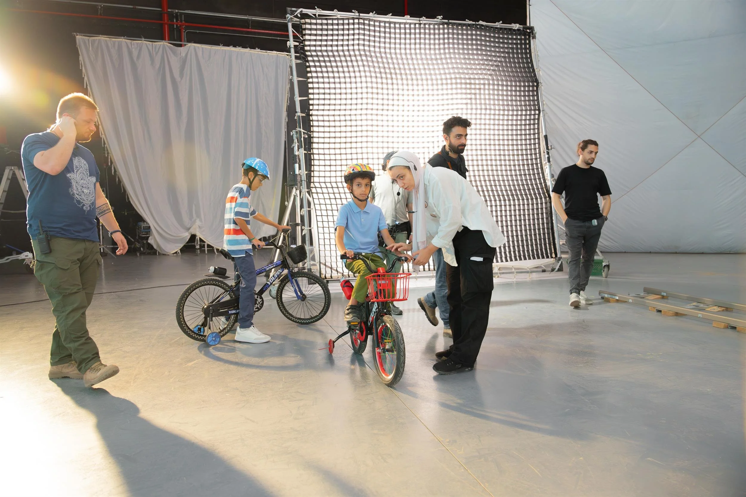 Ahlan Simsim unit still: a crew member adjusts a boy's bicycle while another boy stands beside a blue bike.