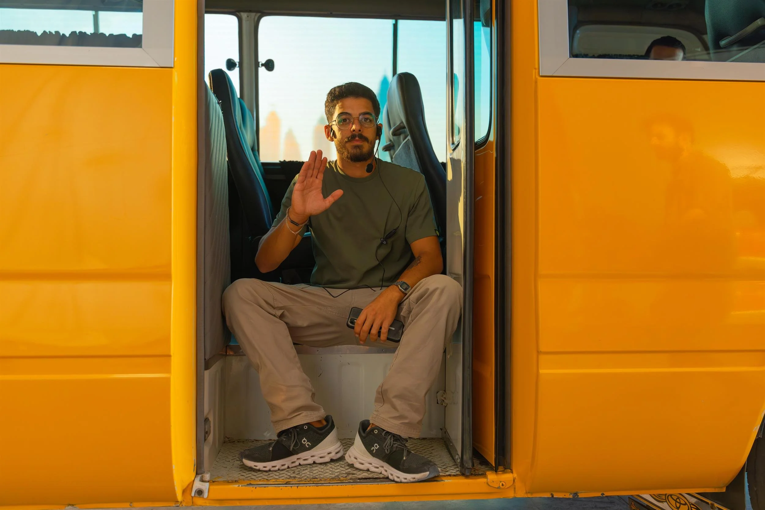 Ahlan Simsim unit still: a crew member with a headset sits in the open doorway of a yellow bus.