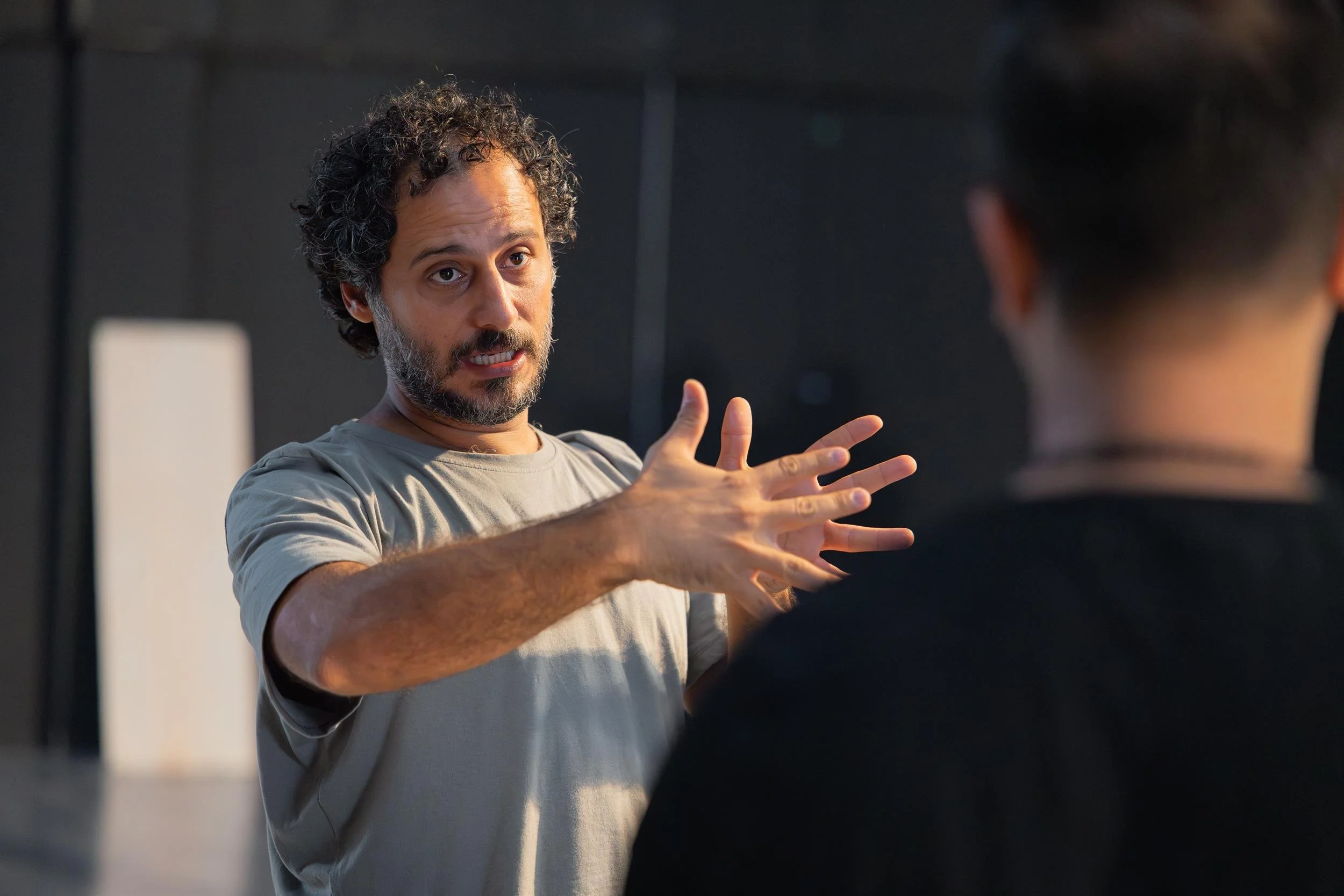 Ahlan Simsim unit still: A crew member with curly hair gestures with his hands while speaking to a colleague in a studio.
