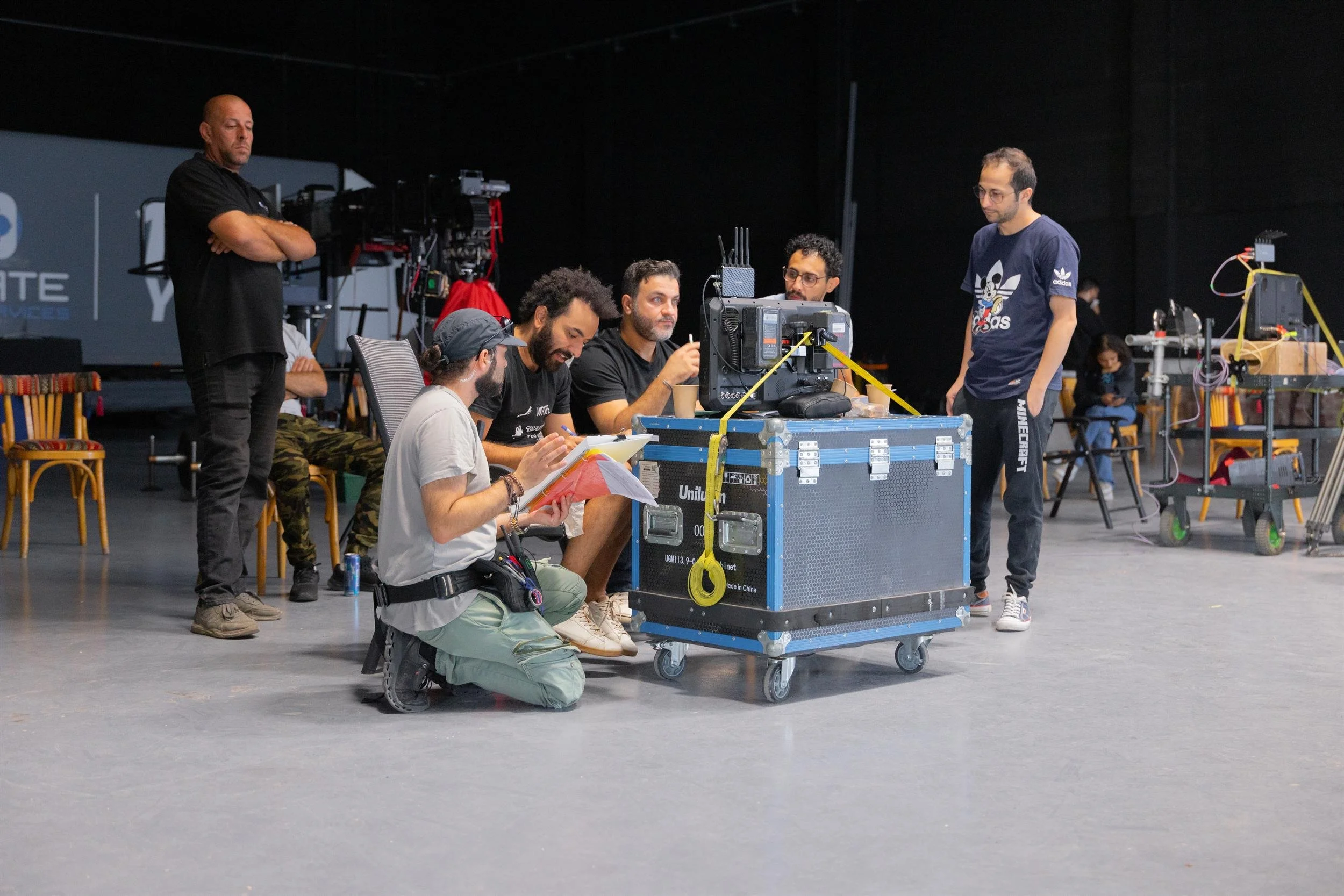 Ahlan Simsim unit still: crew gather around a monitor on a flight case while one kneels with a script binder.