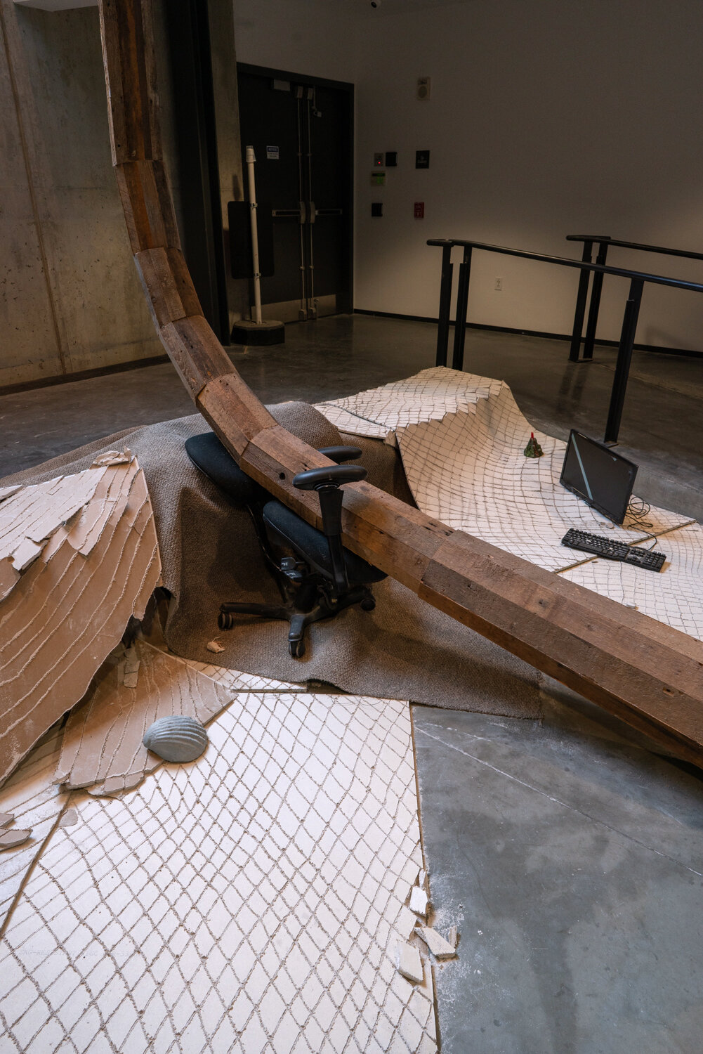  Alex Zak  Swamped , 2019  Sheet rock, plaster wrap, carpet, wood, steel, aluminum, paint, cement, sand, oven-bake clay,   office chair, modified ceiling fan, Monitor, Keyboard, aquarium volcano, red sharpie 192 x 204 x 196 inches (488 x 305 x 498 cm