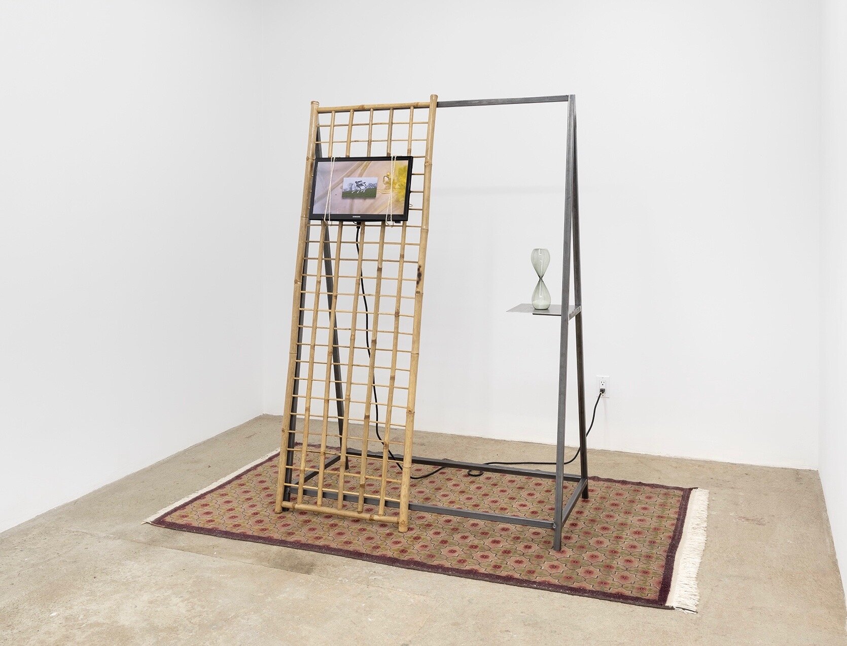  Connor McNicholas  Every Portal , 2020 Steel, bamboo, rug, television, hourglass, cables, electricity, hardware  86 x 48 x 70 inches (219 x 122 x 178 cm) TRT: 1 hour, 22 minutes 